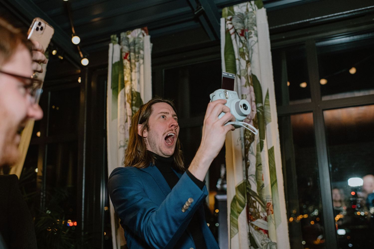 Person in blue taking photos with excitement at an indoor event.