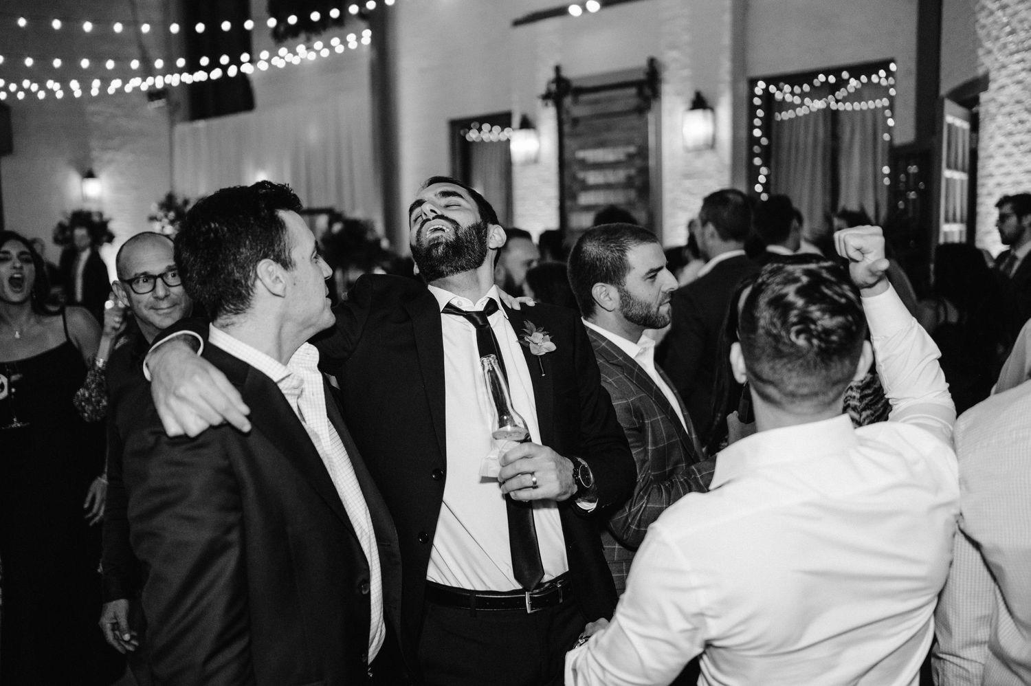 Party guests dancing and celebrating at a wedding reception under string lights.
