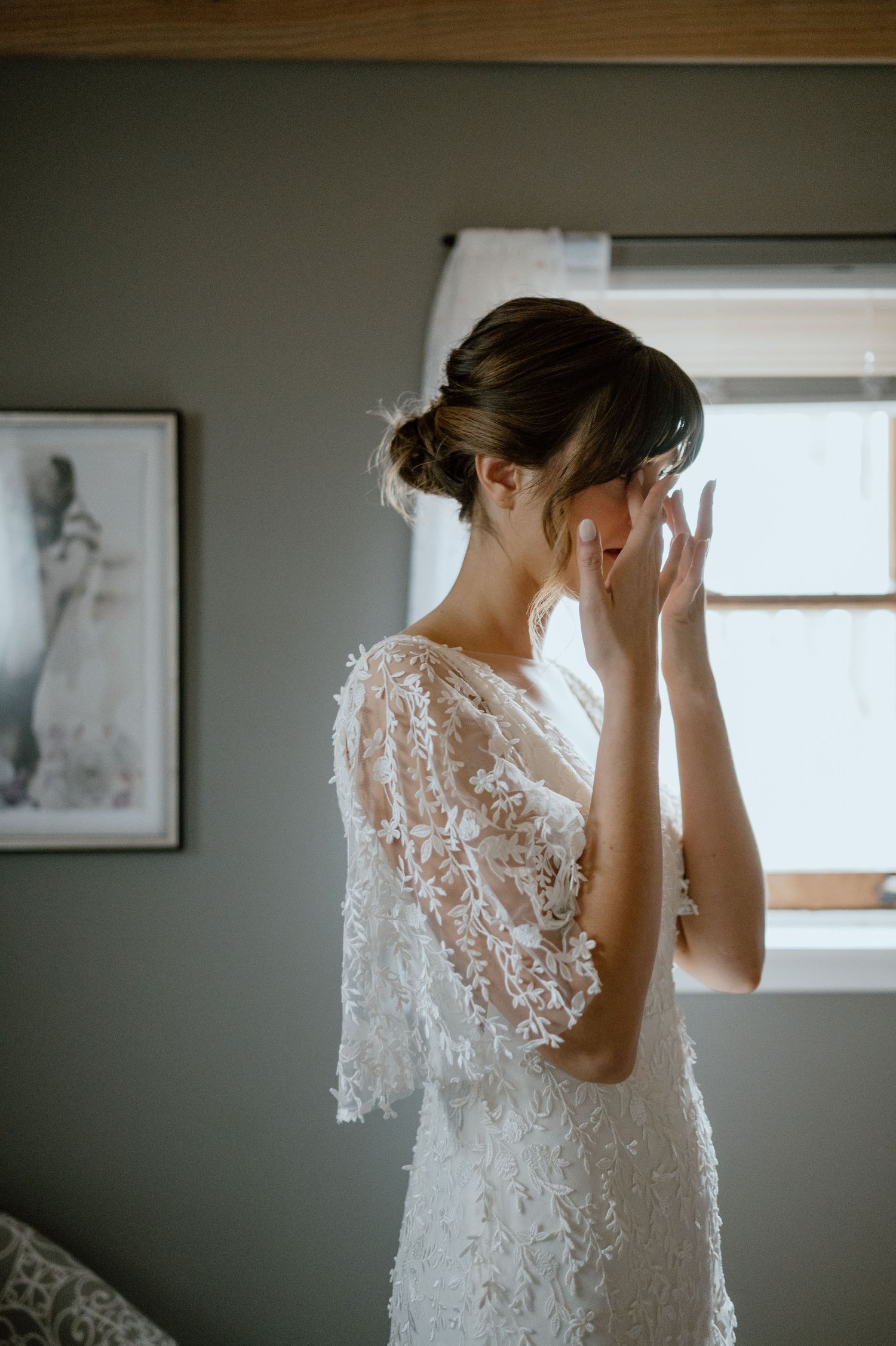 Ethereal side profile of a bride in a delicate lace wedding dress by a window.