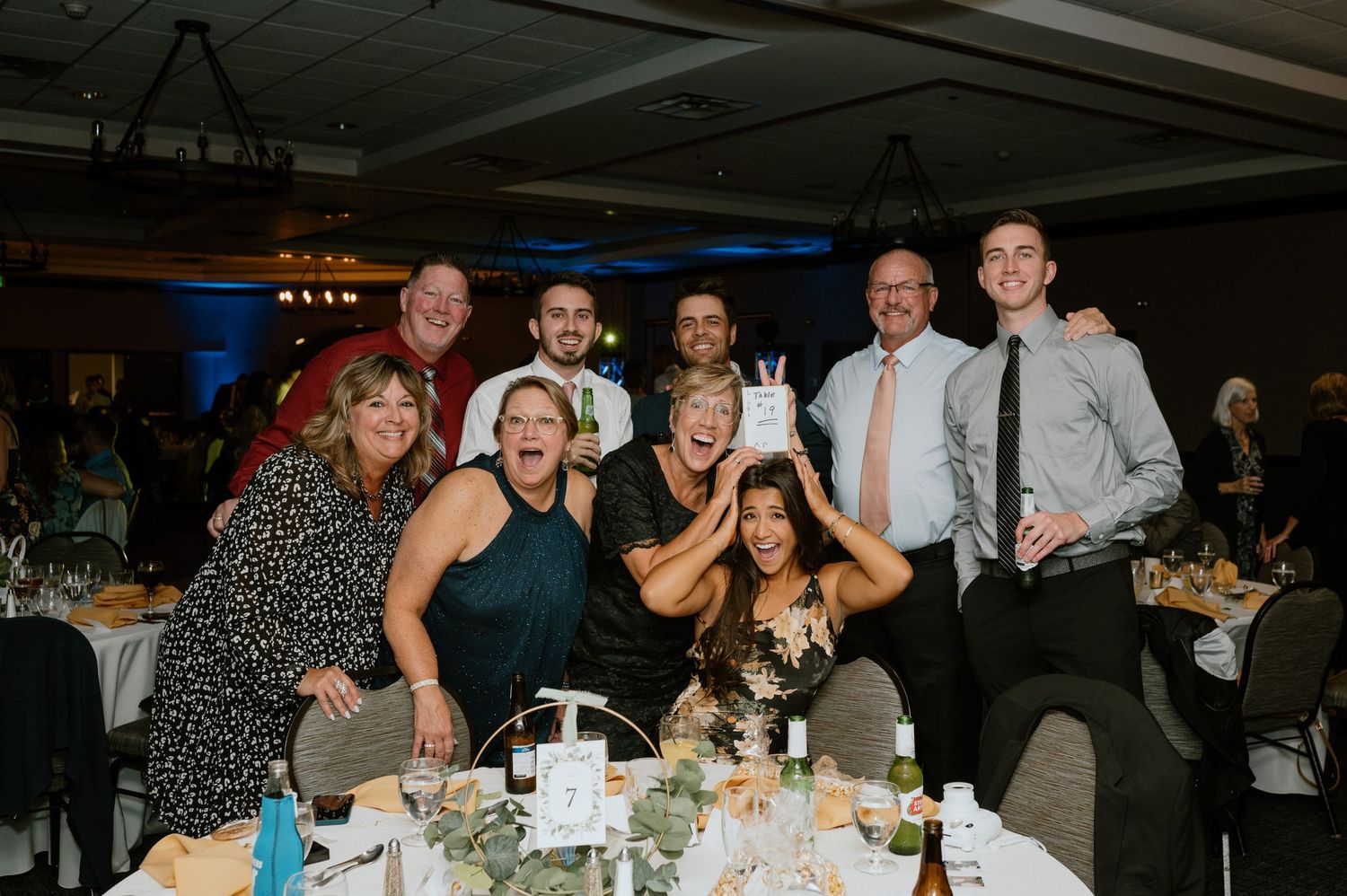 Group of wedding guests posing enthusiastically at reception table.