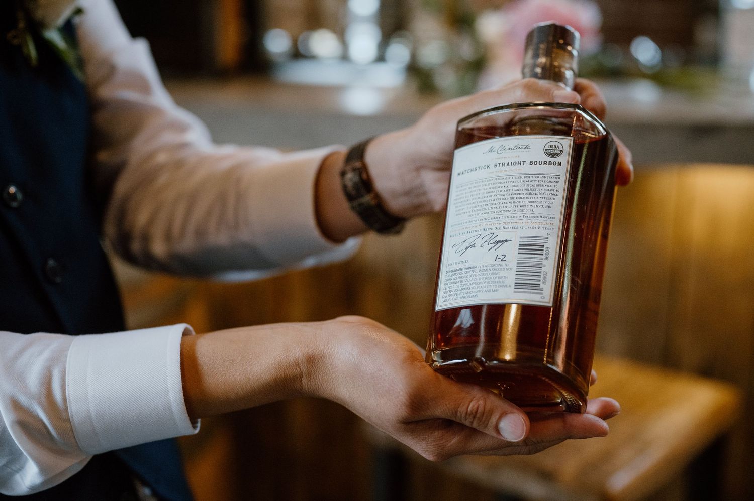 Hands holding a bottle of whiskey in a distillery tasting room.