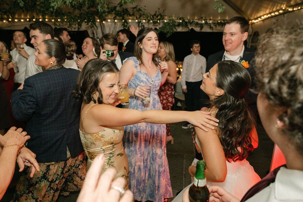 Guests dancing and celebrating at a dimly lit wedding reception with string lights overhead.
