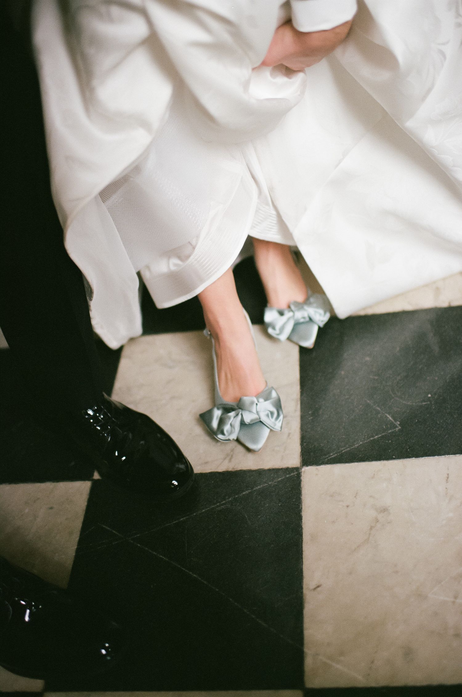 Close-up of blue bridal shoes peeking out from under a white wedding dress.