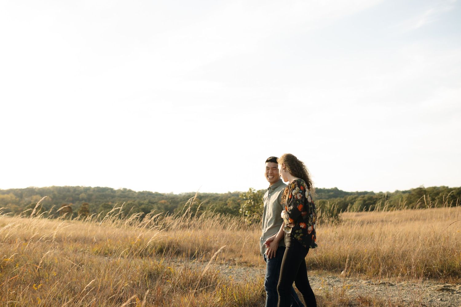 A couple walking together through golden prairie grass at sunset.