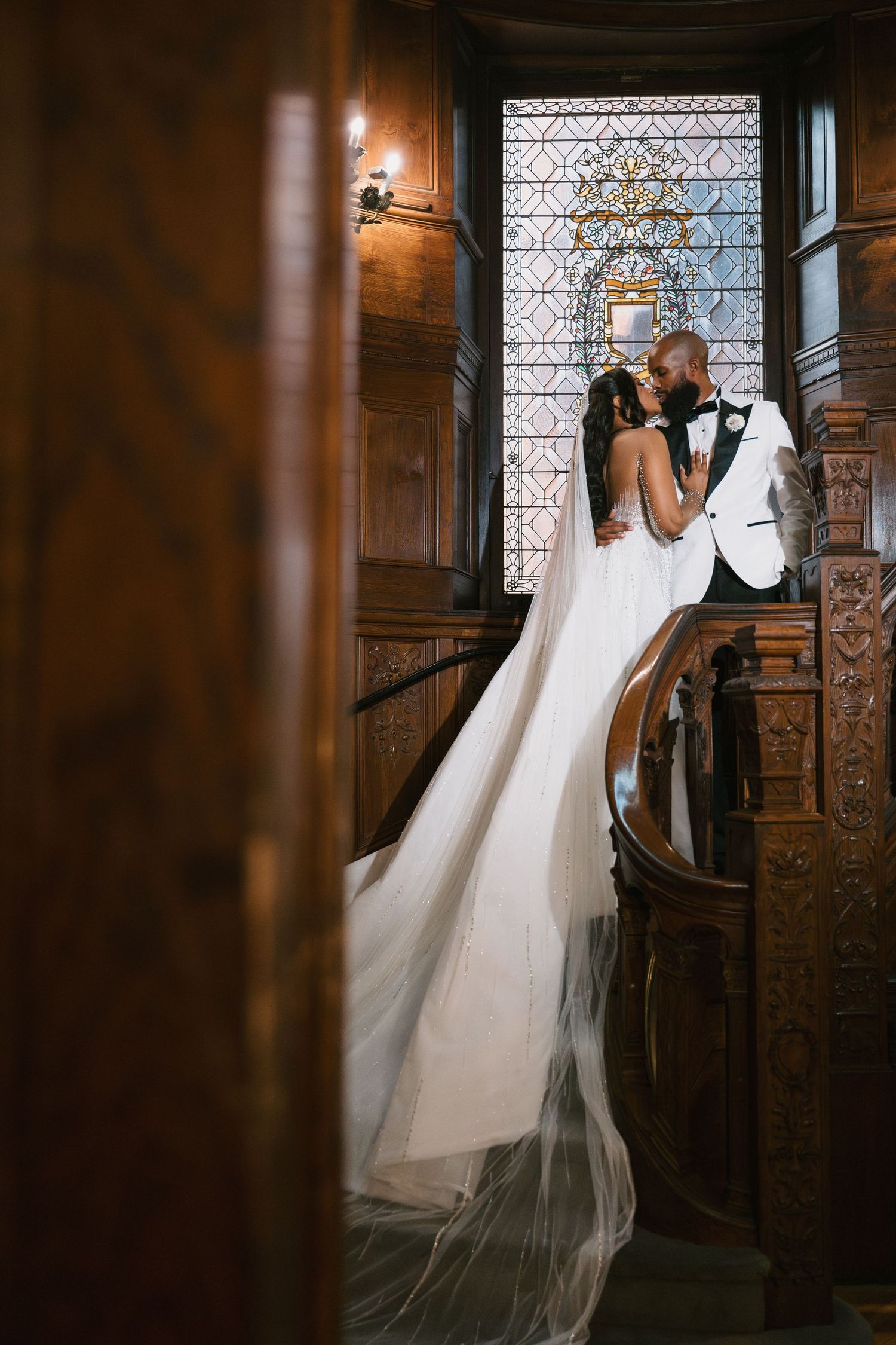 A flowing white wedding dress train cascades down an elegant wooden staircase in a historic mansion.