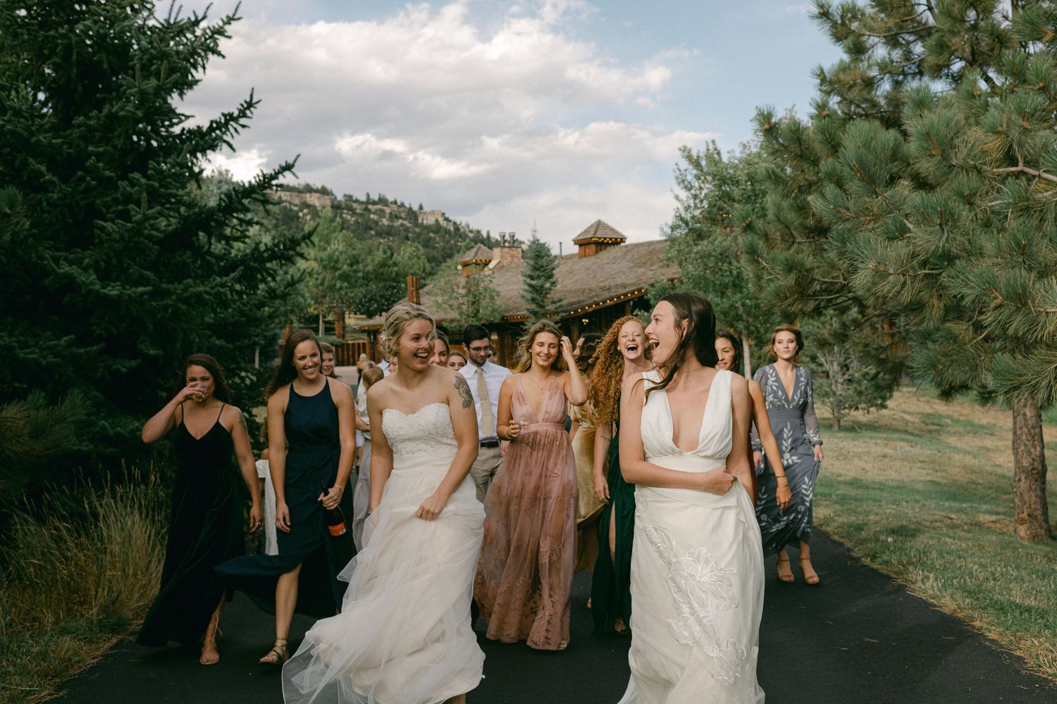 Wedding party walks down path surrounded by evergreen trees in mountain setting.