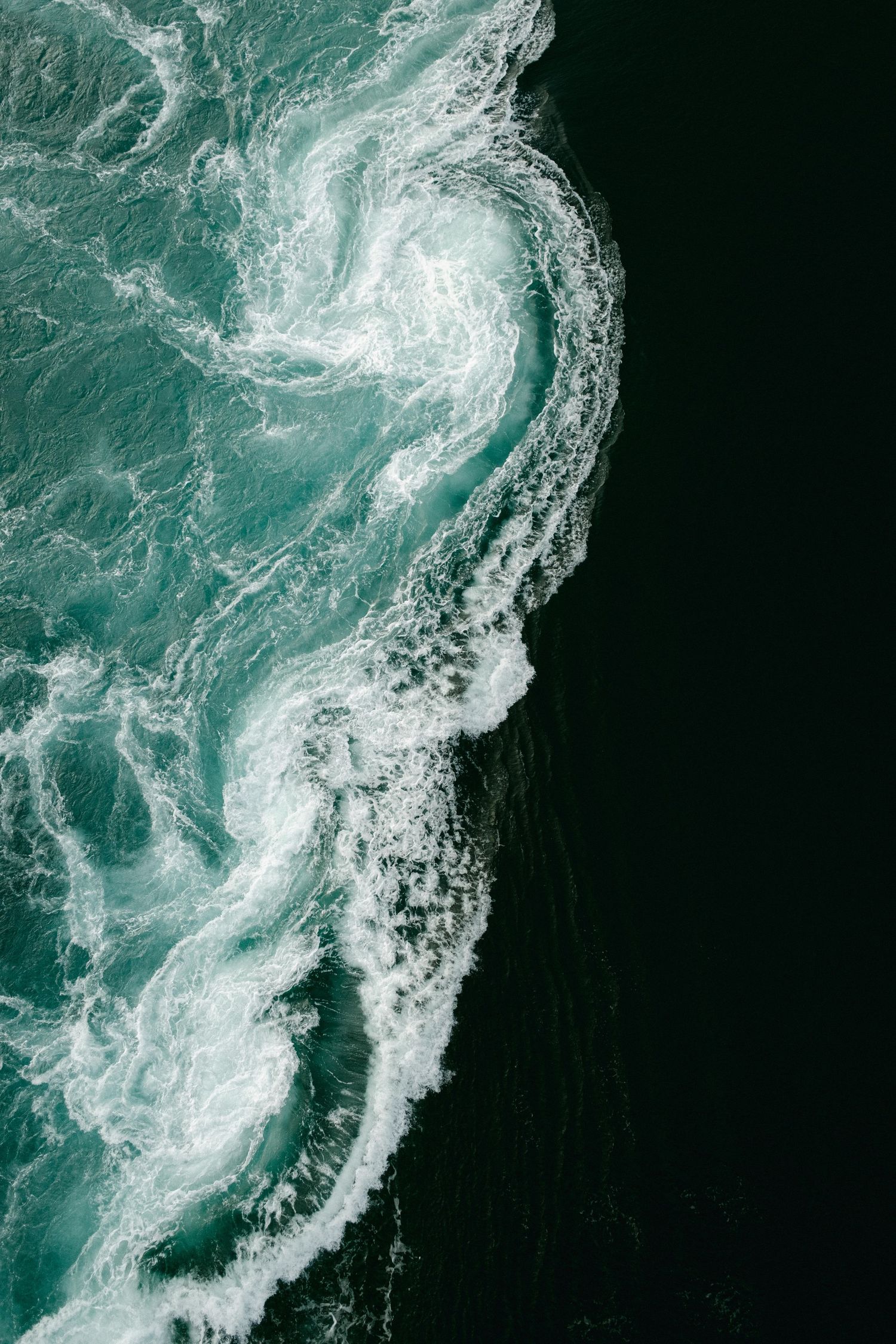 Aerial view of swirling turquoise ocean waves creating dramatic patterns against dark water.
