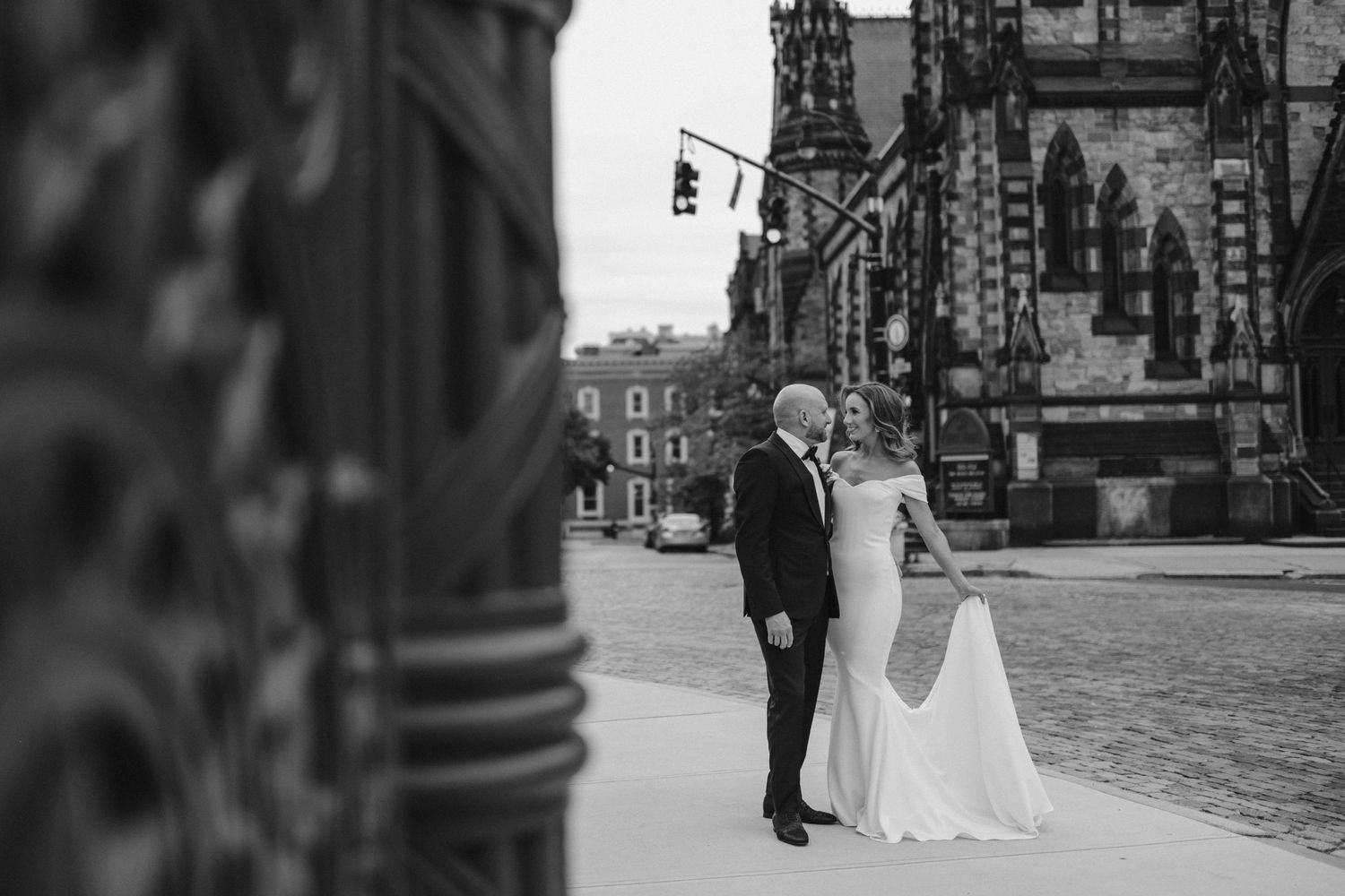 Black and white photo of newlyweds standing near historic architecture.