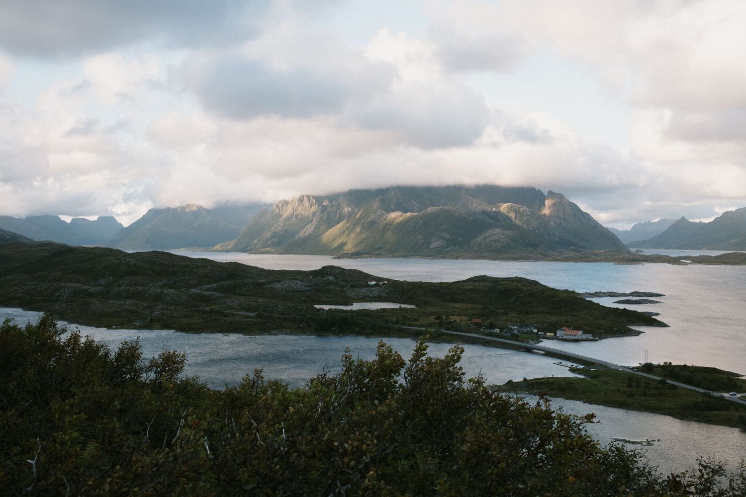 Misty fjord landscape with mountains reflecting in calm waters under cloudy skies.