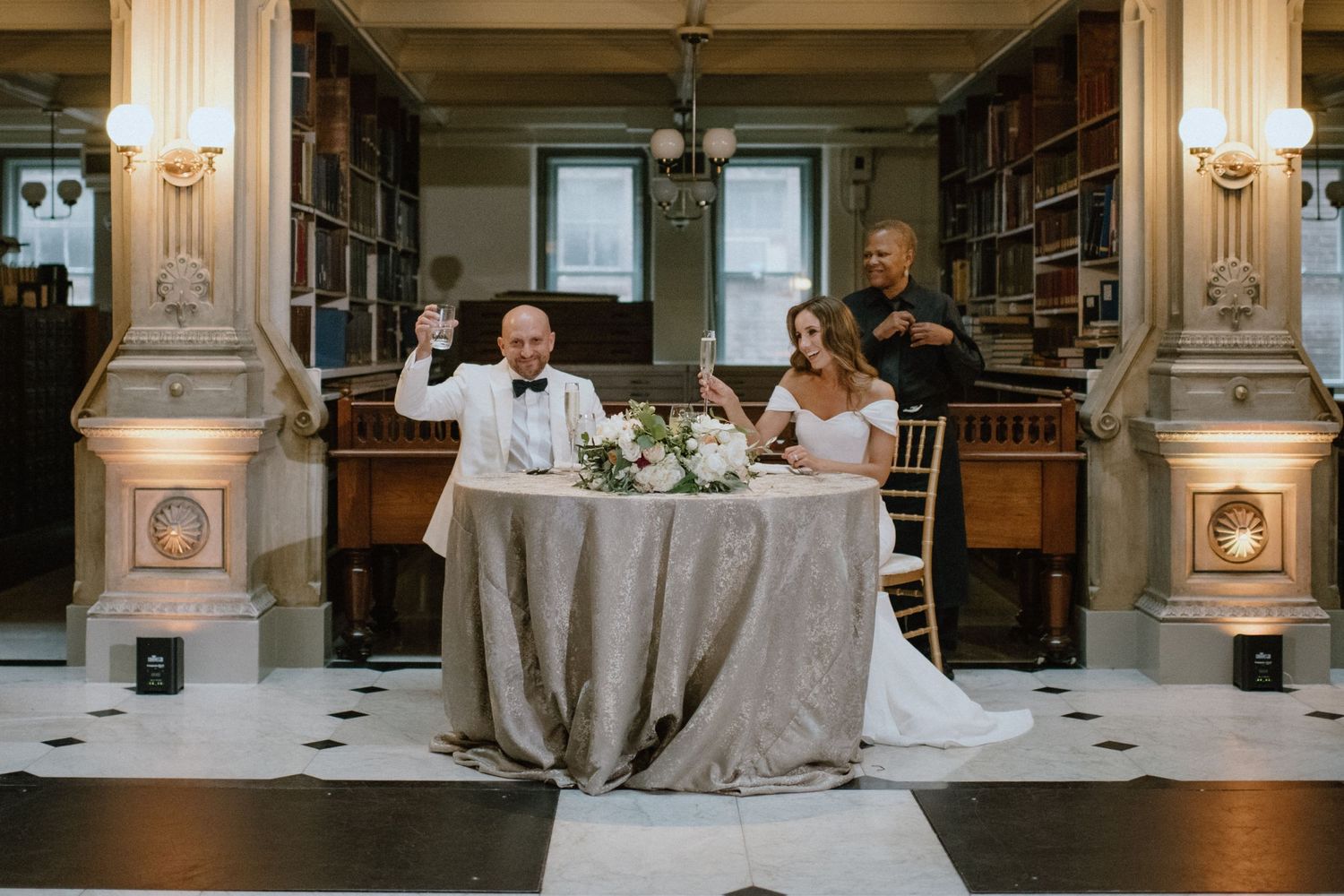 Wedding reception table setup in historic library with classical columns and checkered floor.