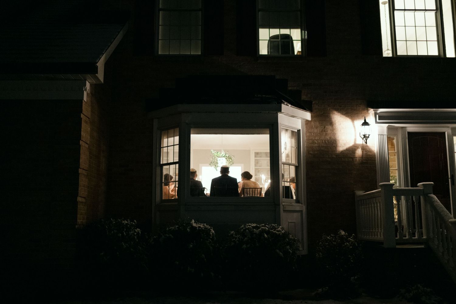 Silhouetted figures seen through window at nighttime wedding celebration.