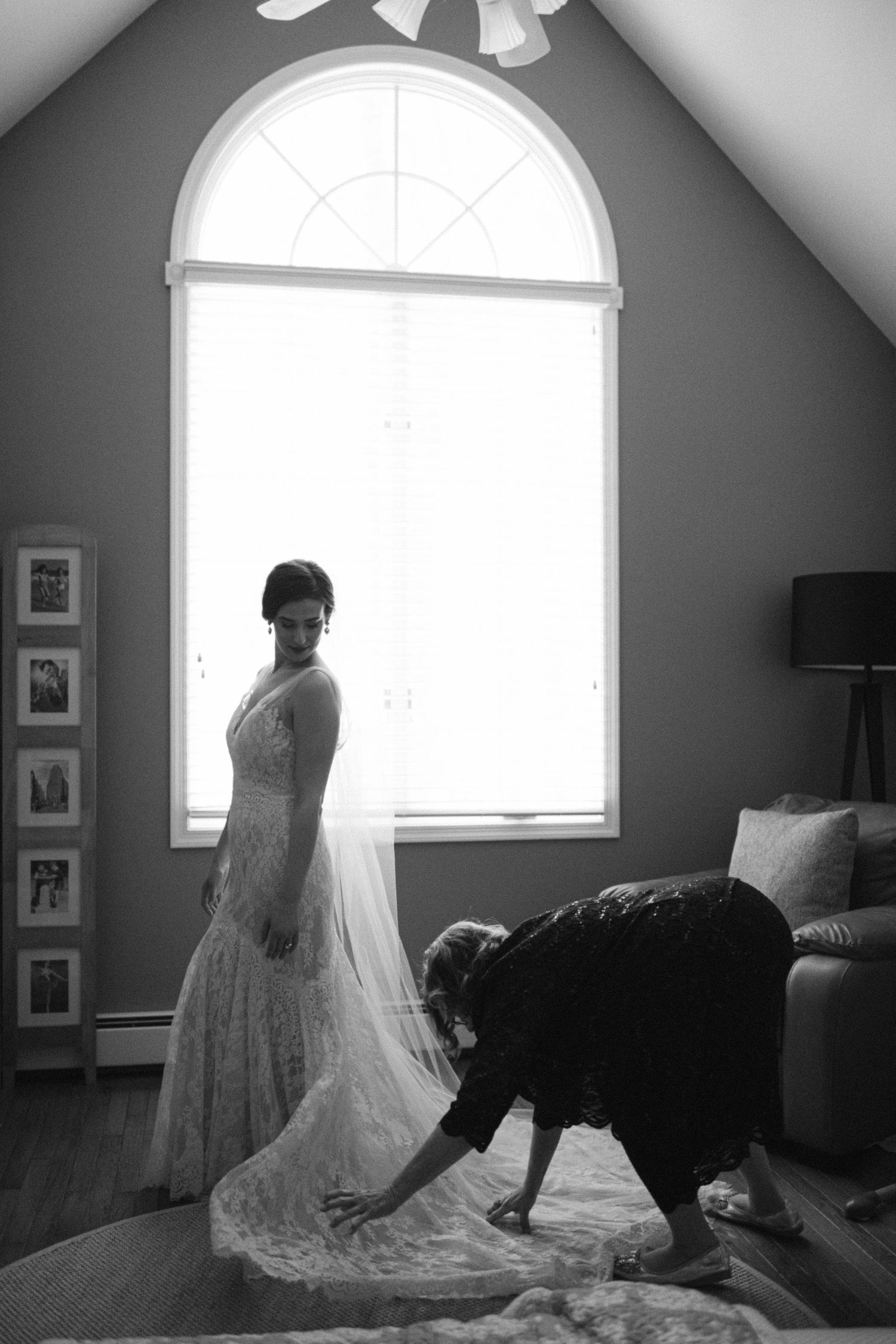 Black and white photo of wedding dress preparations near a large arched window.