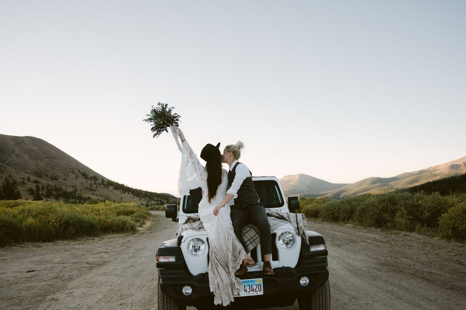 A couple celebrates on their white Jeep during a mountain wedding photoshoot.