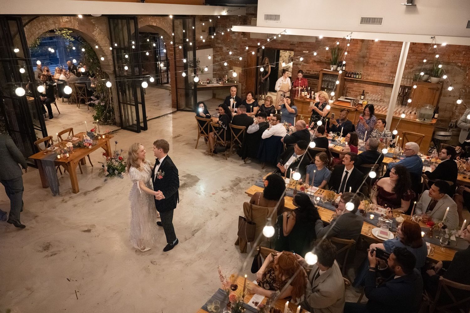 Overhead view of wedding couple's first dance surrounded by seated guests in an industrial venue.