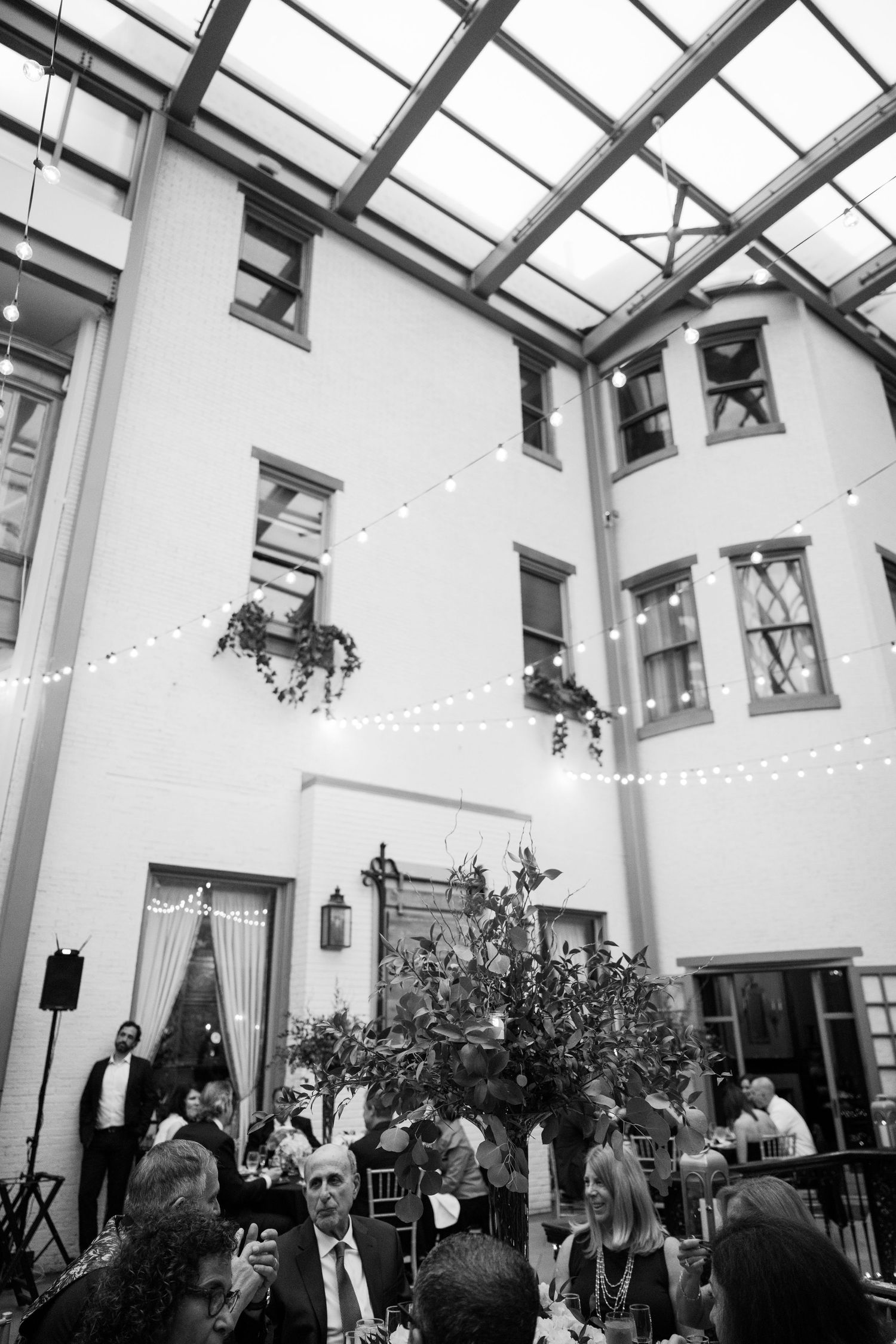 Black and white photo of courtyard reception with string lights and multiple stories of windows.