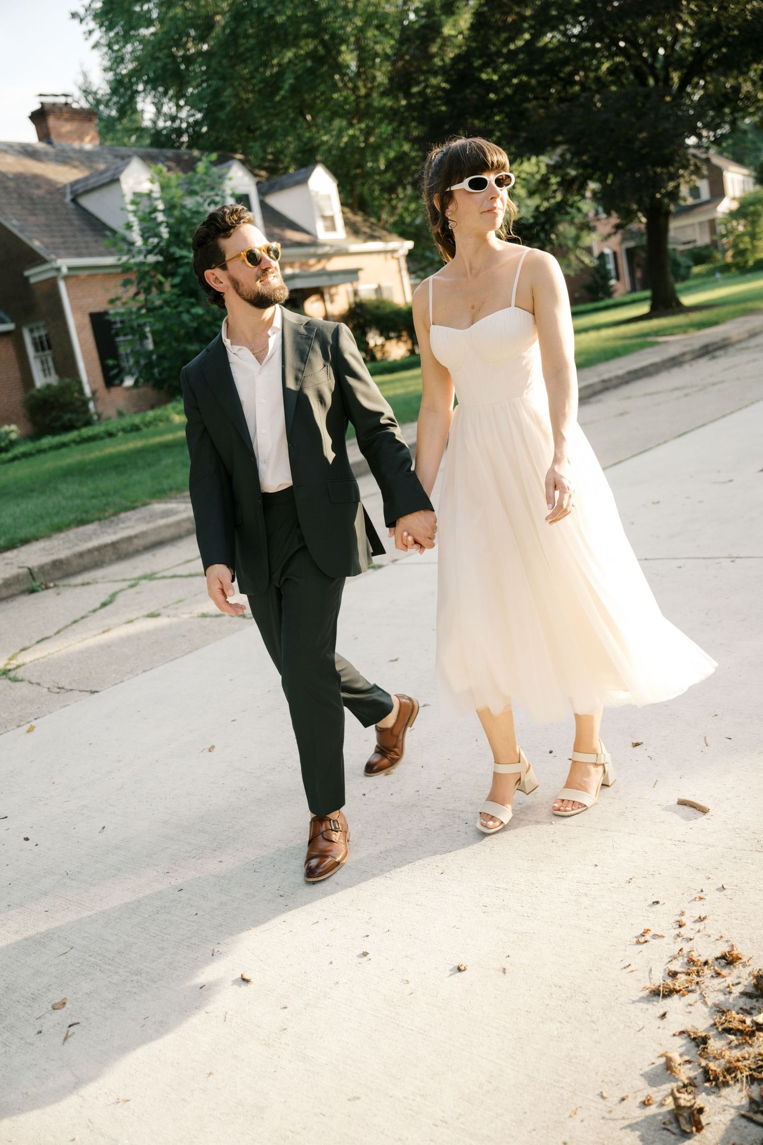A couple walking together on a sidewalk, with her in a white summer dress and him in a dark suit.