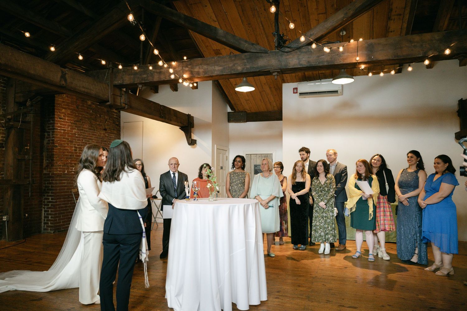 Wedding reception venue with string lights and exposed brick walls filled with celebrating guests.