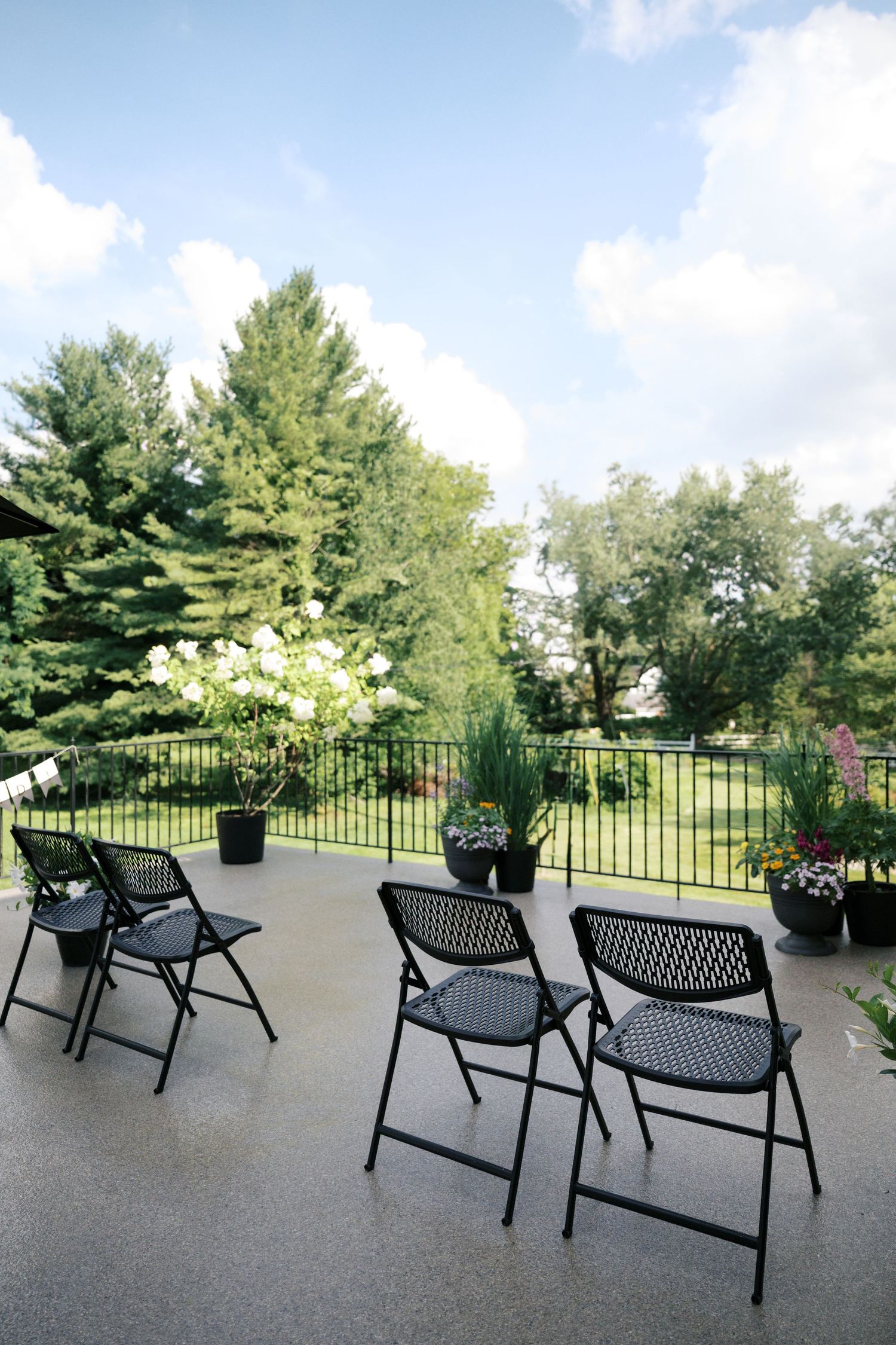 Black metal outdoor lounge chairs arranged on a patio deck with green trees and blue sky in the background.