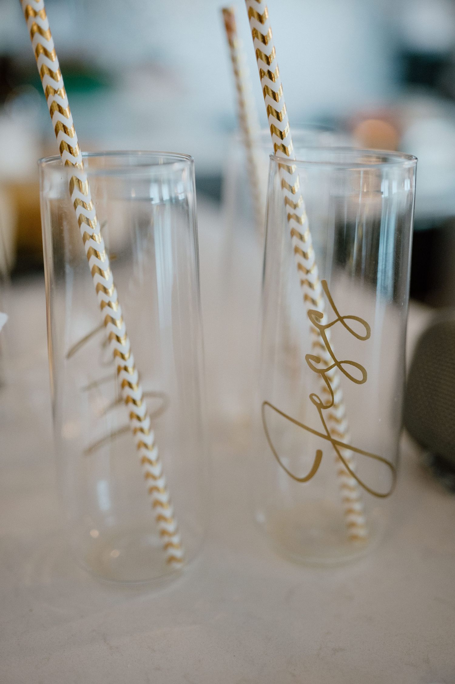 Two drinking glasses with gold striped straws and elegant script writing.
