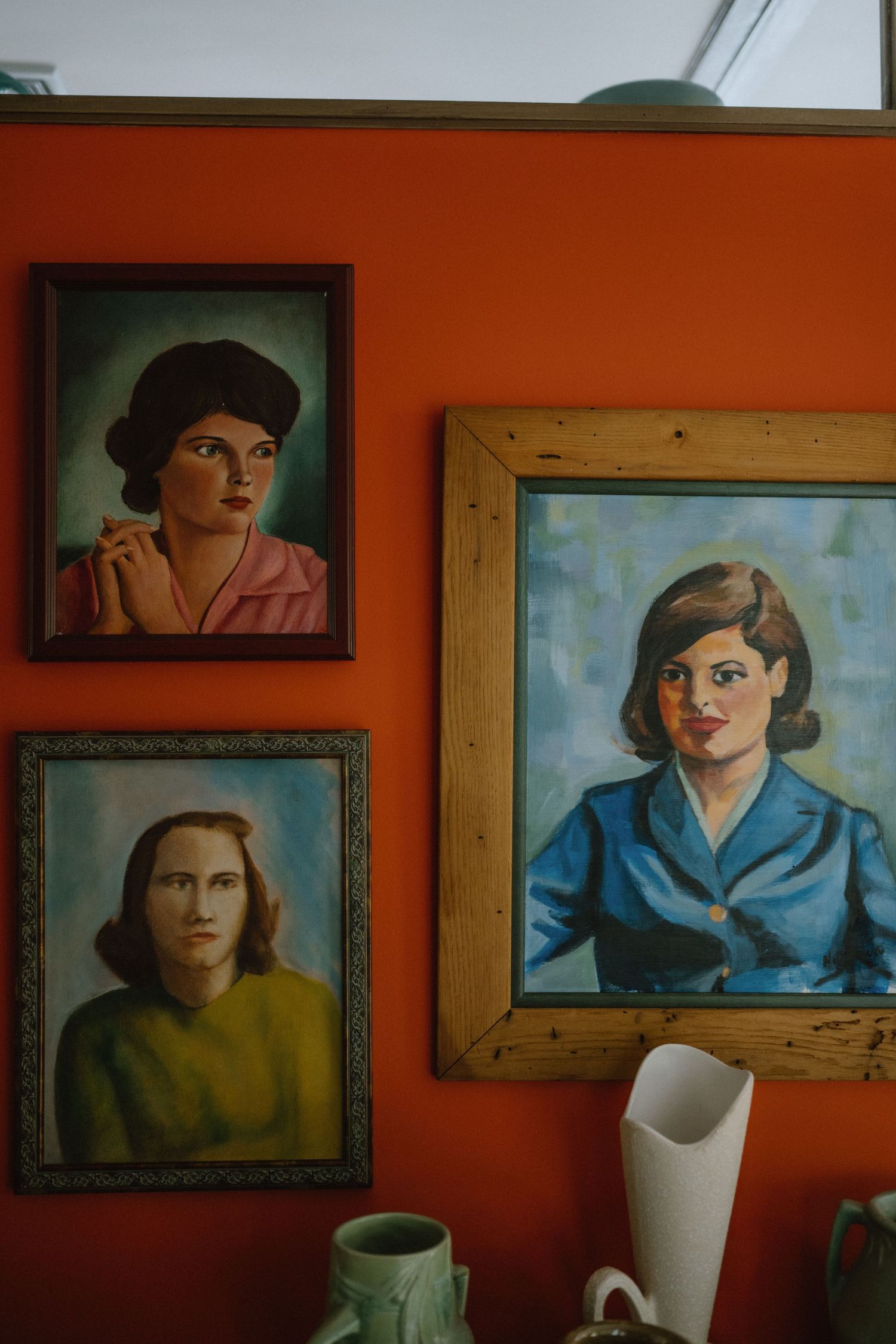 Vintage portrait paintings on bright orange wall with ceramic vases below.