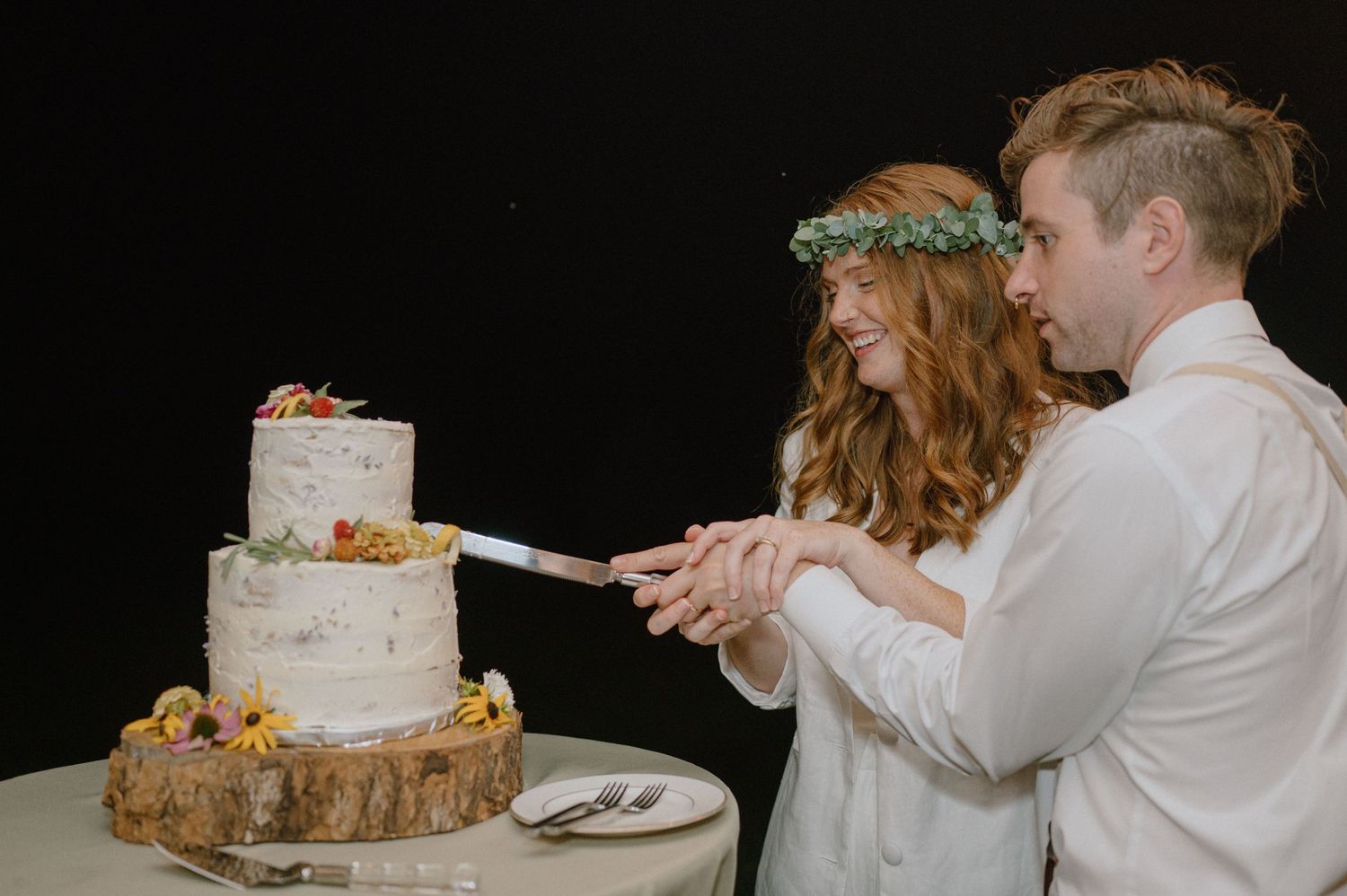 A couple cuts their rustic wedding cake displayed on a wooden slice.