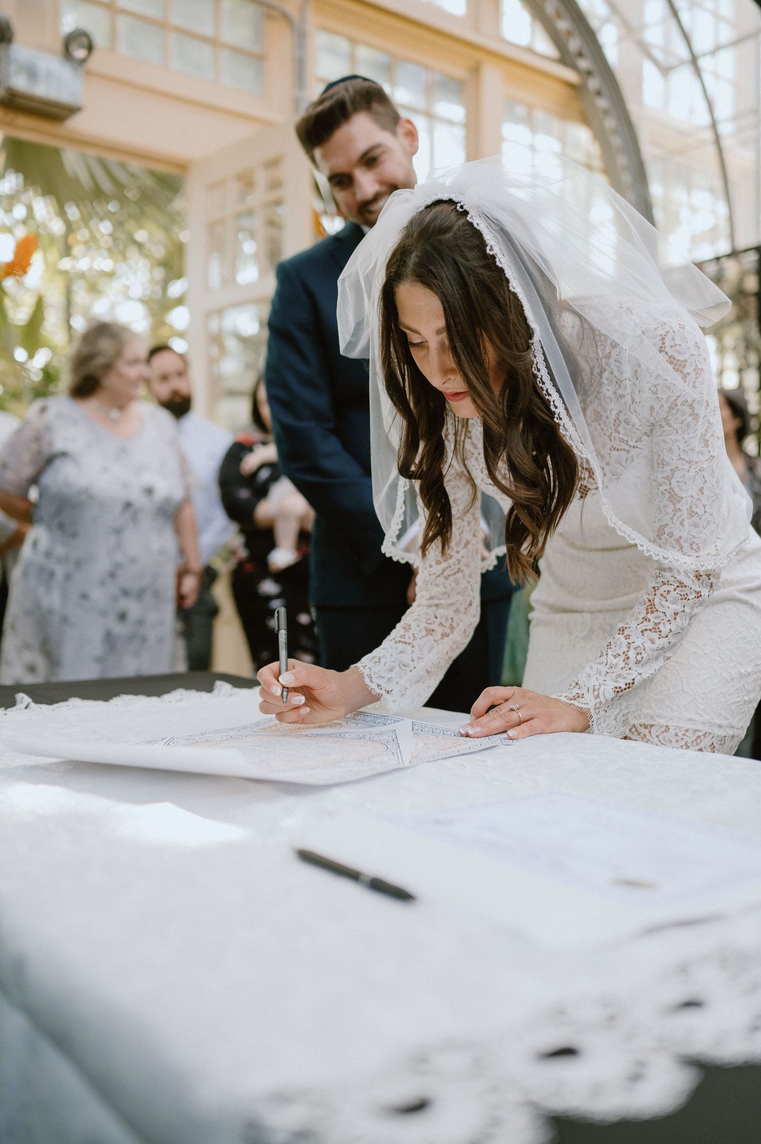 Bride signs marriage document during greenhouse wedding ceremony.