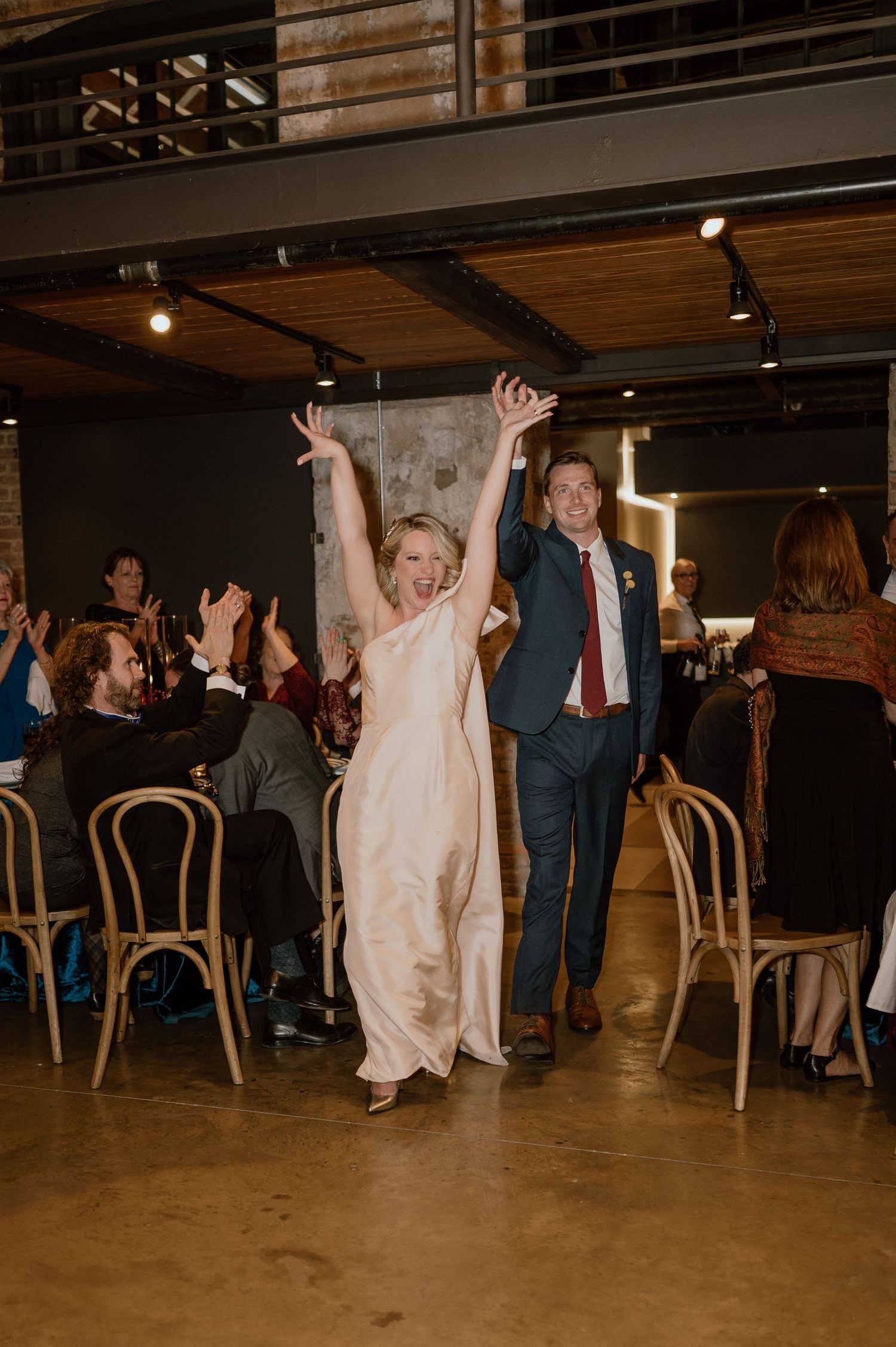 Celebratory moment at a reception with guests dancing in an industrial-style venue with string lights.