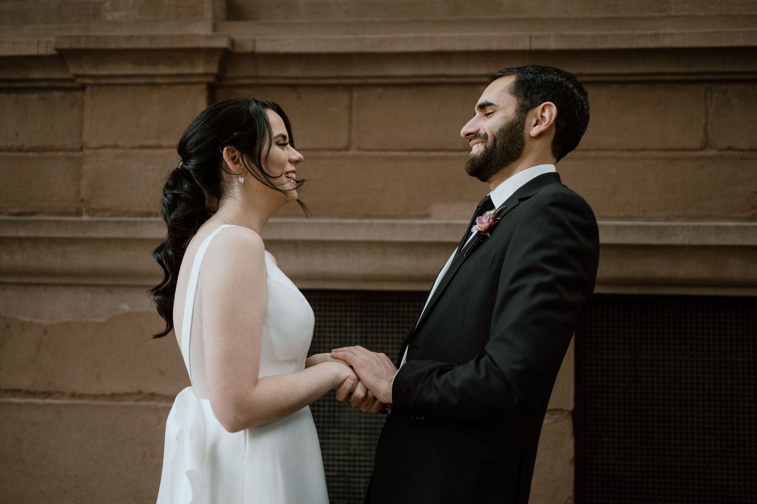 A candid moment between newlyweds holding hands and laughing together outside.