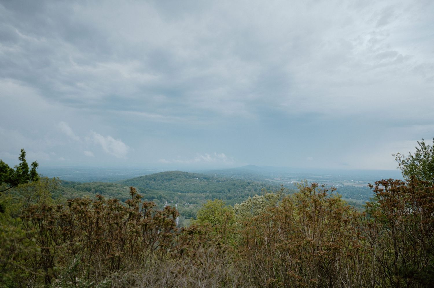Misty mountain landscape with rolling hills stretches beneath cloudy blue skies.