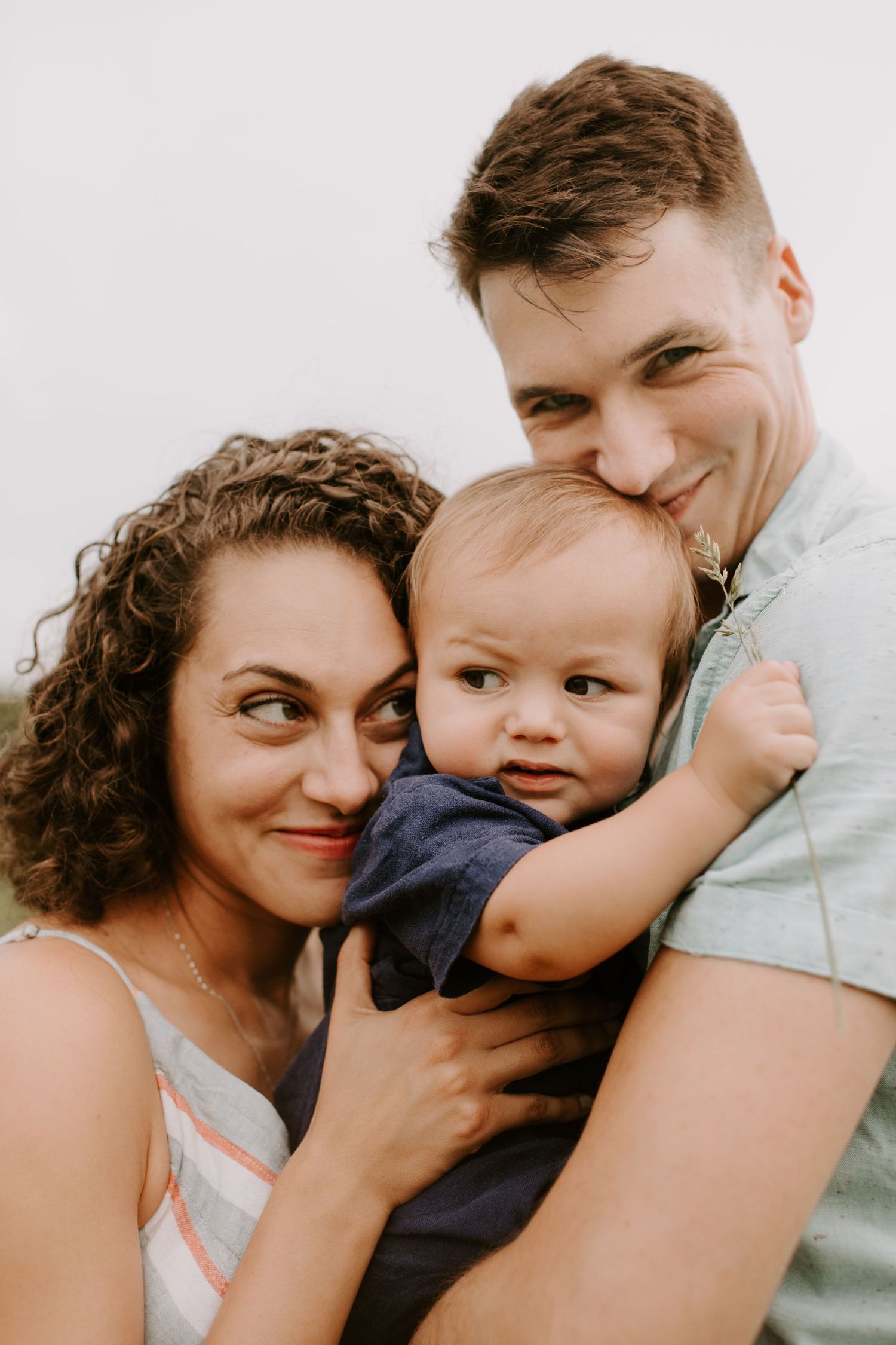 Joyful family portrait with small baby in navy outfit being held closely between parents.