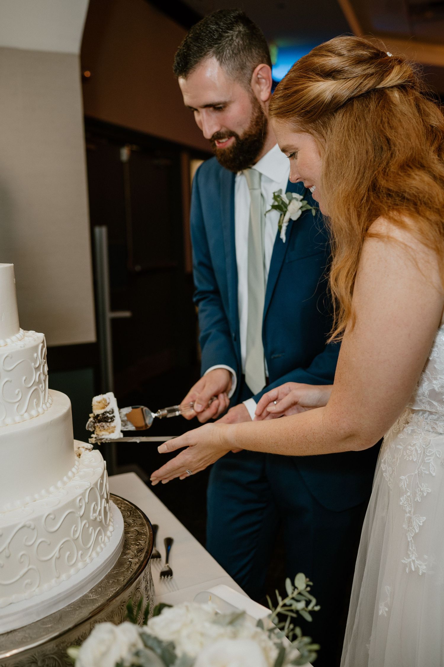 Wedding couple cuts into their elegant white tiered cake during the reception.