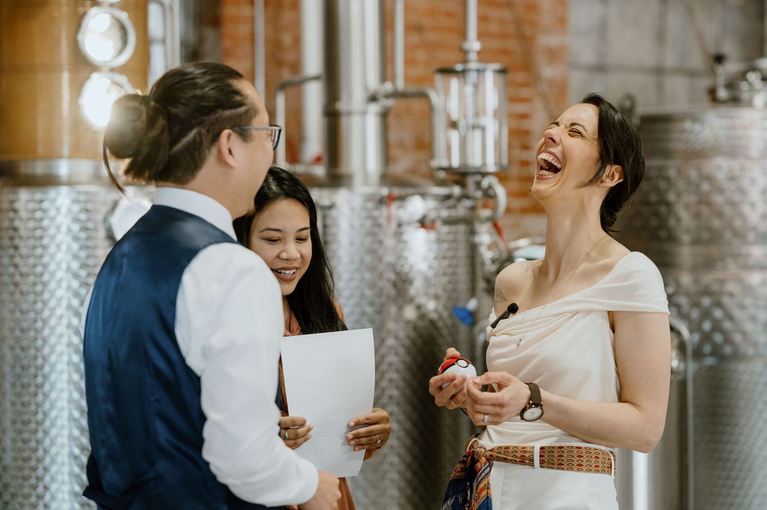 A joyful moment during a ceremony in front of industrial distillery equipment.