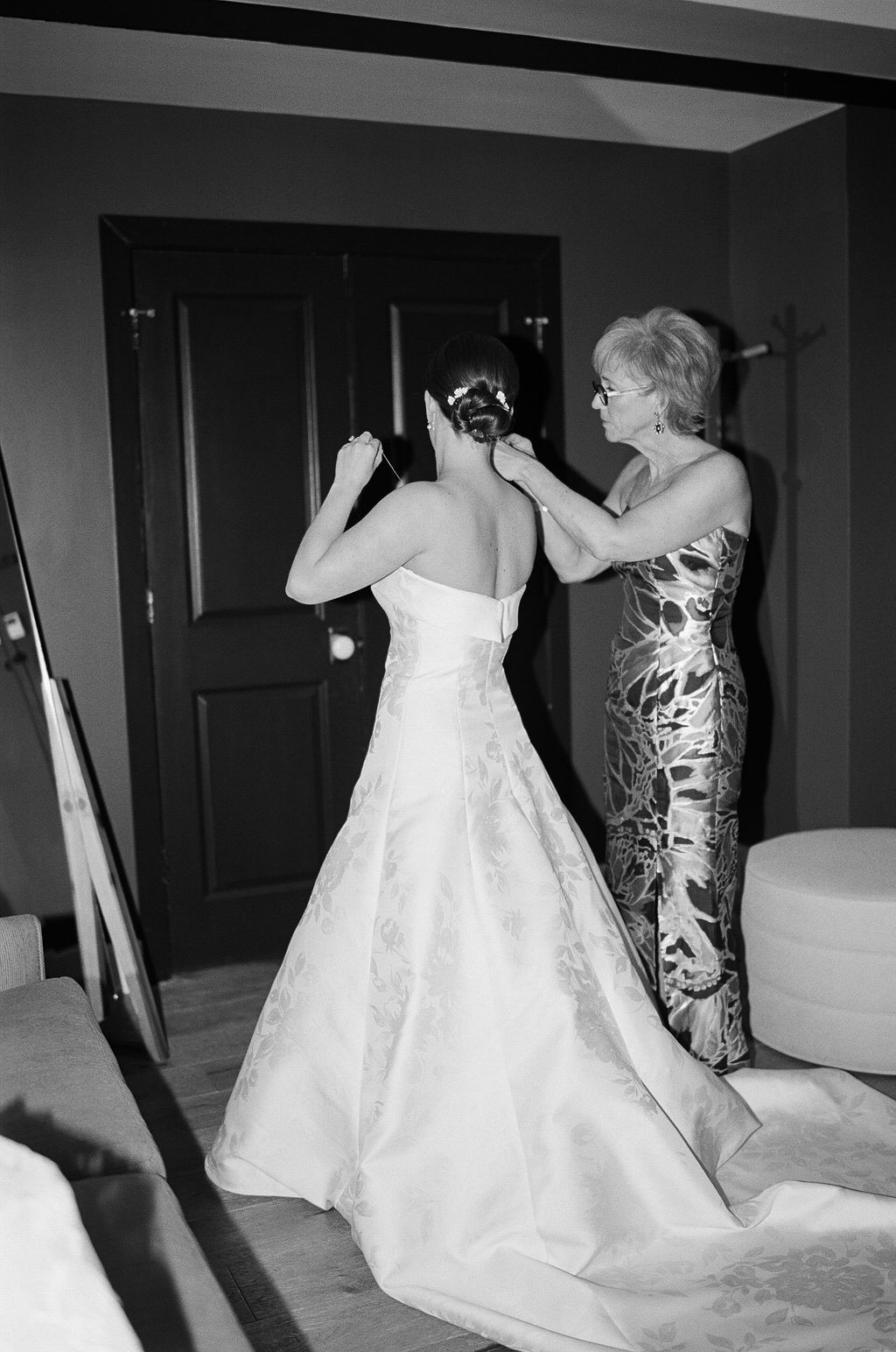 Black and white image of wedding dress preparations with bridesmaids assisting.