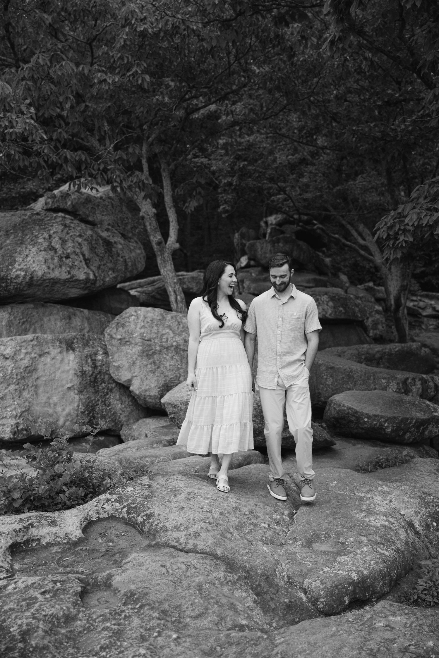 Black and white image of couple exploring rocky terrain surrounded by trees and natural landscape.
