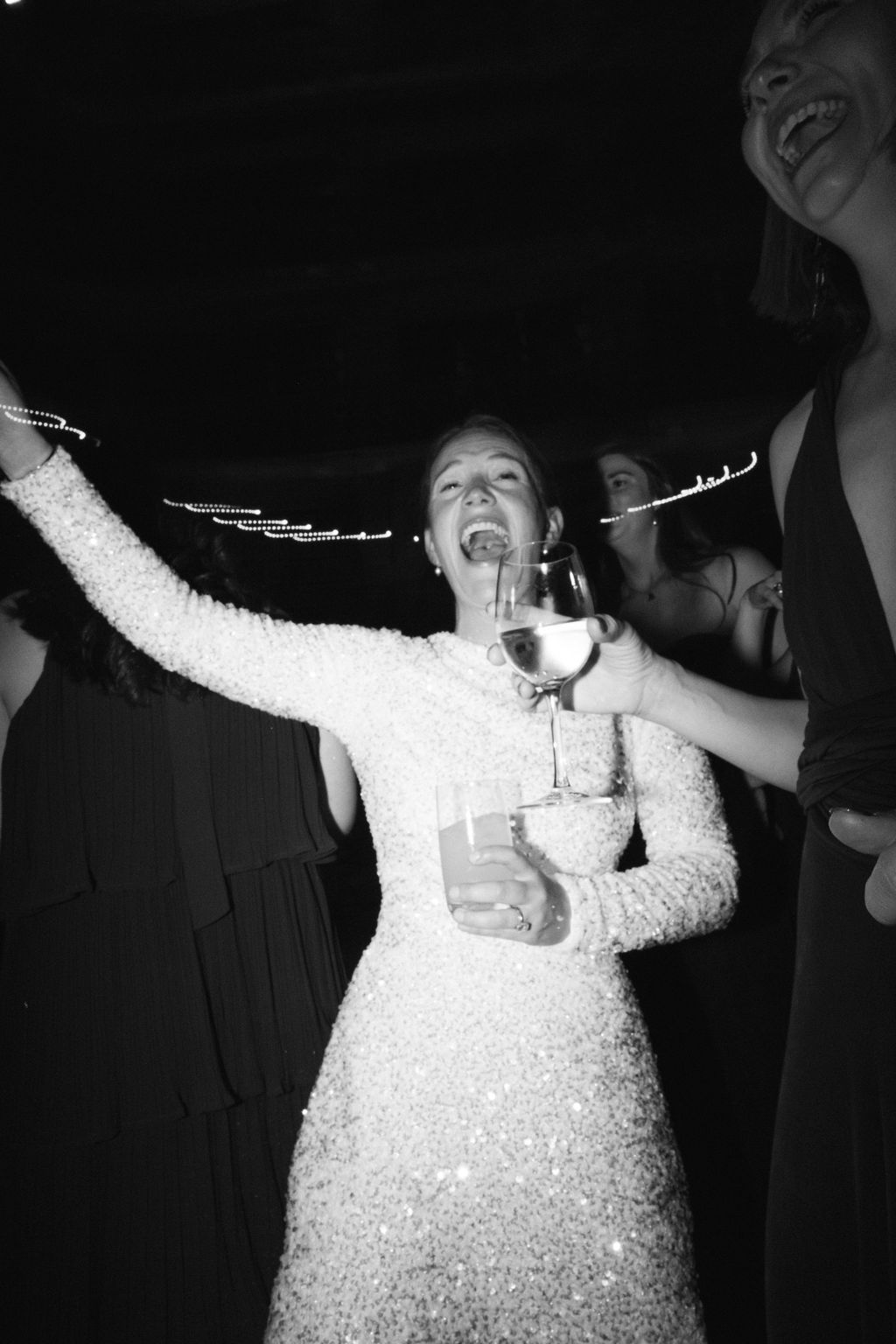 Person in white dress celebrating with arms raised during wedding reception dance party.