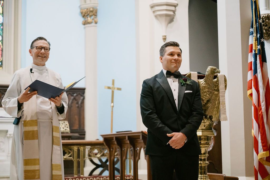 Wedding ceremony taking place in a traditional church sanctuary with ornate stained glass windows and white columns.