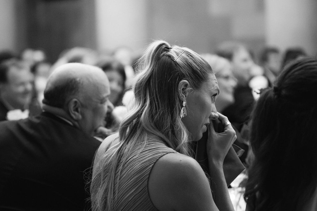 Black and white photo of a person with a ponytail laughing in a crowded indoor event.