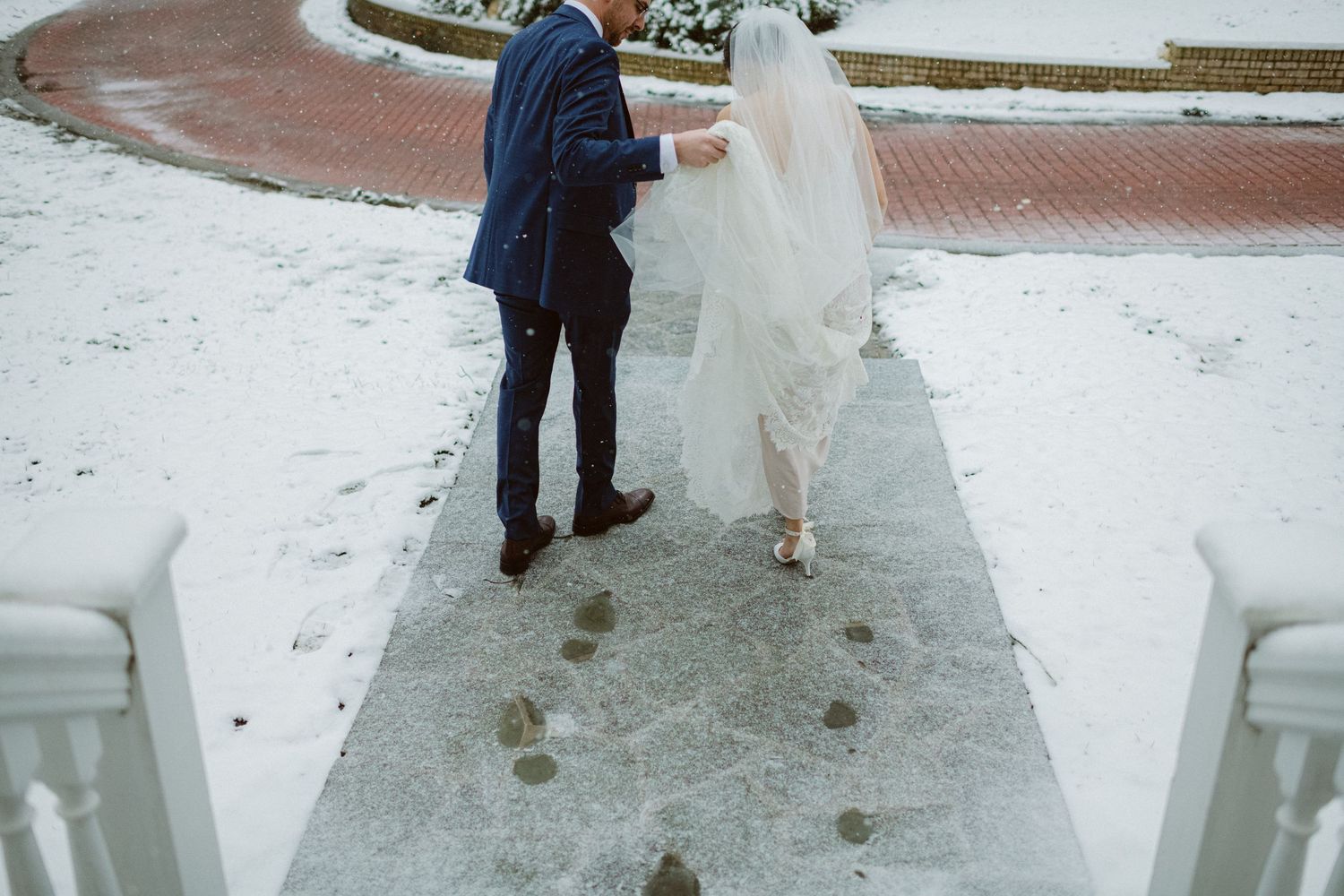 A couple walks through snow on a winter wedding day, leaving footprints behind.