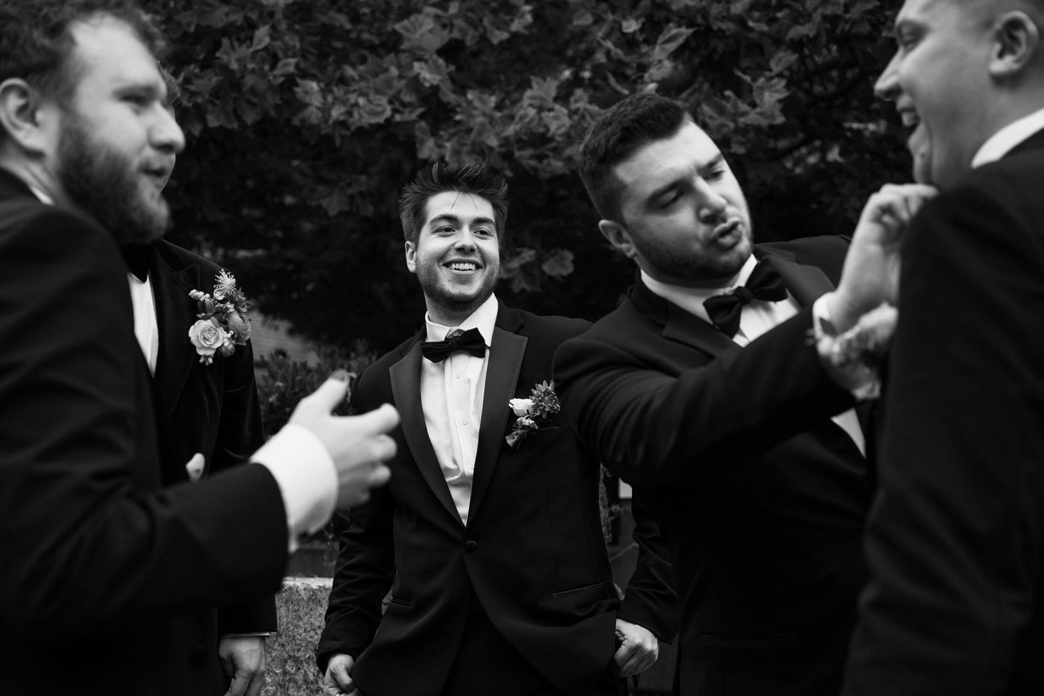 Groomsmen share a candid black and white moment of laughter during wedding festivities.