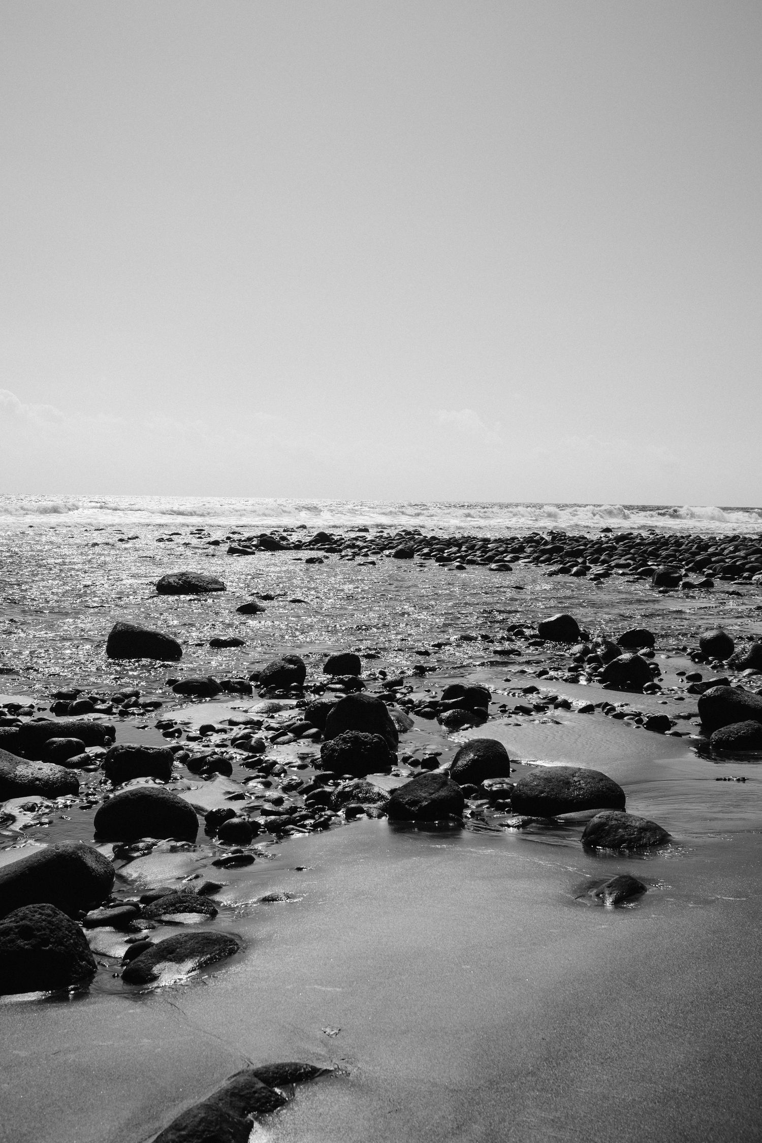 Black and white photo of rocky shoreline with waves crashing against stones.