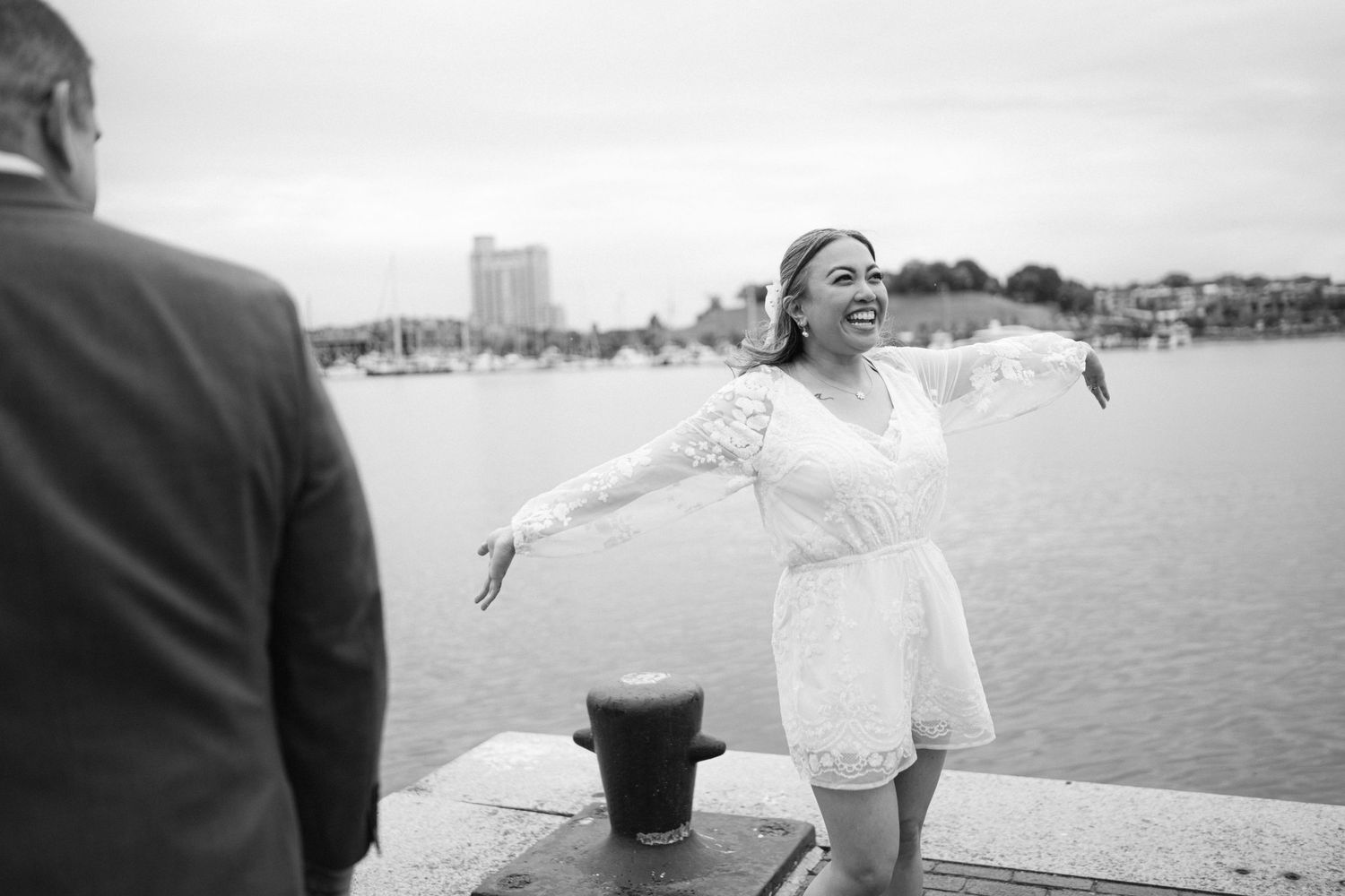 A couple shares a joyful moment on a waterfront pier with the harbor in the background.