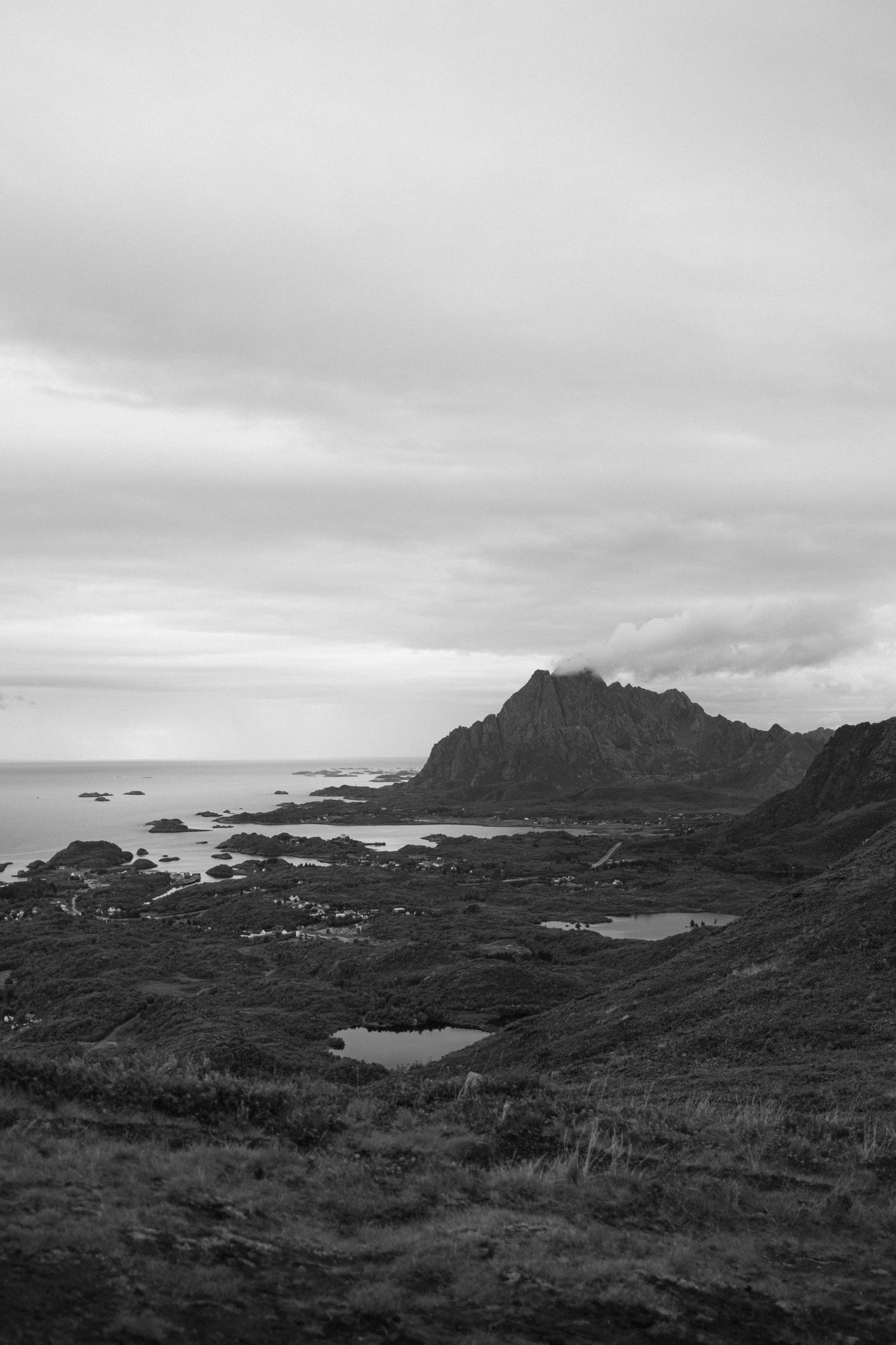 Dramatic black and white coastal landscape with rocky cliffs and scattered pools along a rugged shoreline.