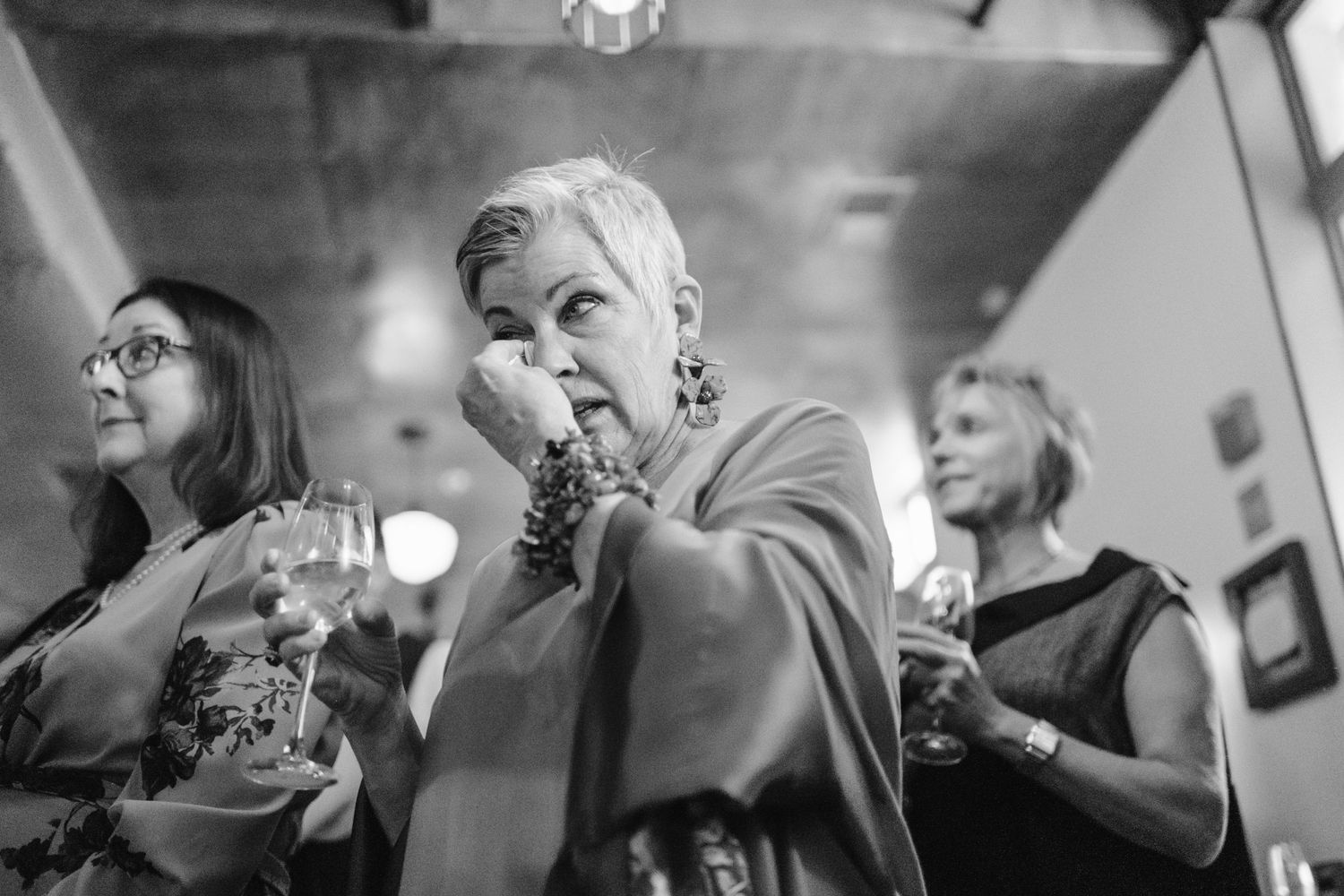 Black and white photo of wedding guests sharing laughter and emotional reactions.