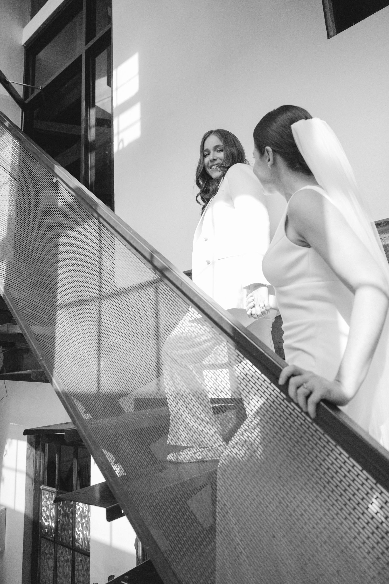 A person in white clothing ascends a modern glass and metal staircase in a contemporary interior setting.