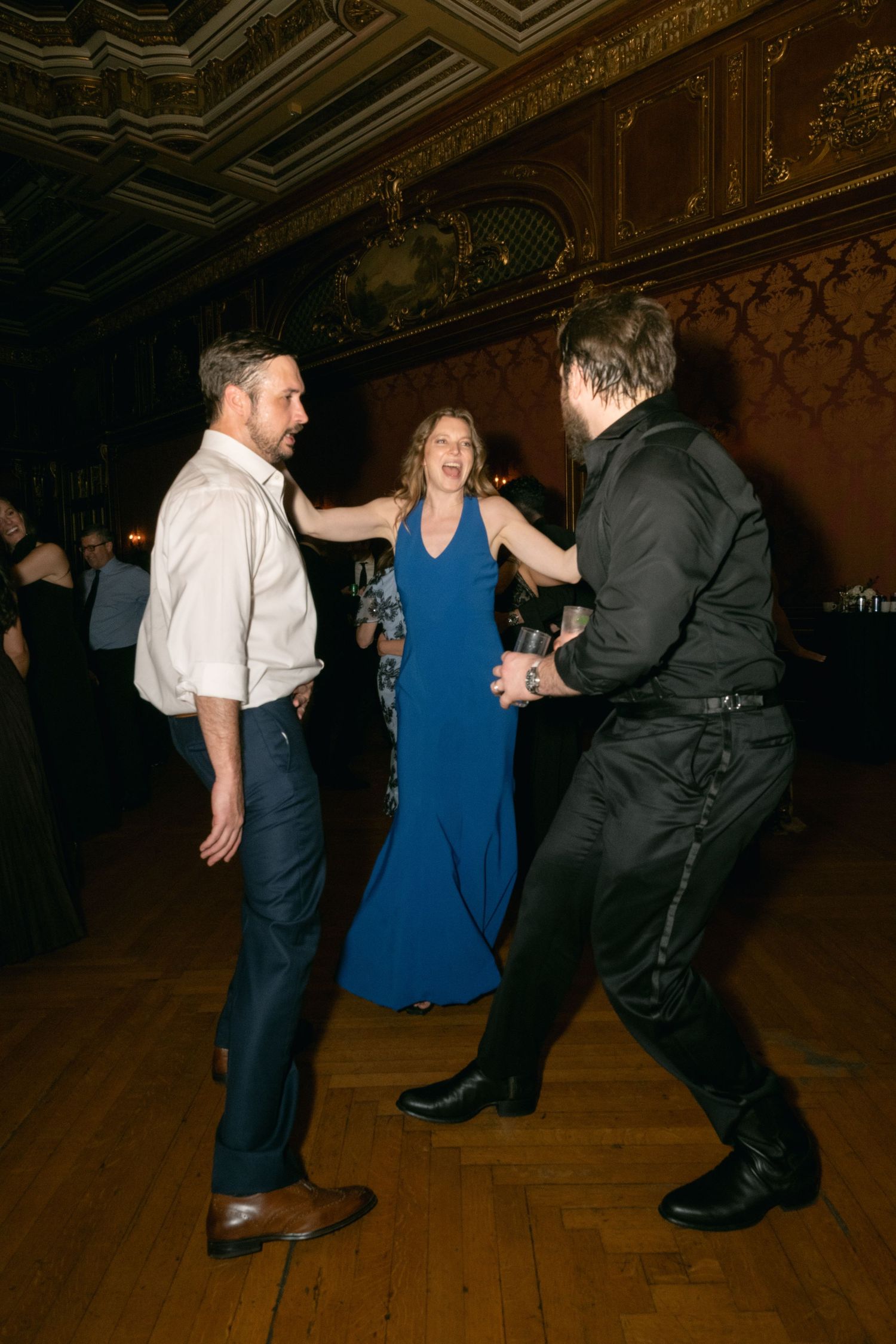 People dancing together at an elegant party in a historic venue with ornate walls and ceiling.