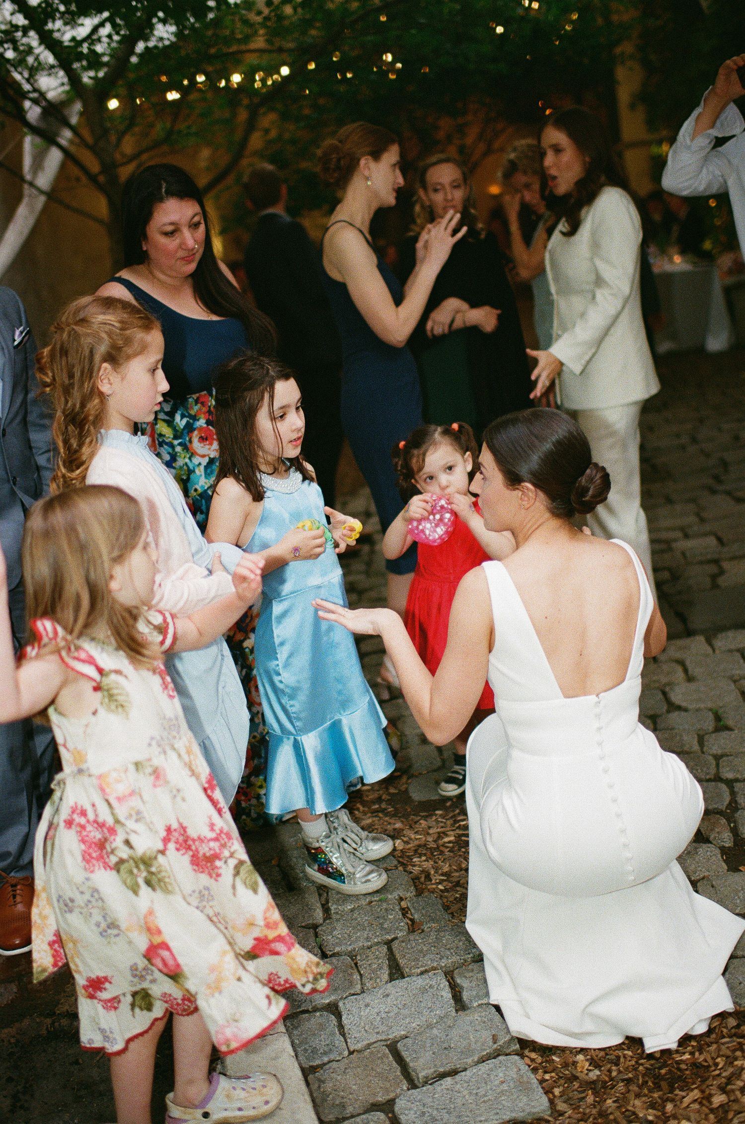 Children and adults dancing together on cobblestone pavement at an outdoor wedding celebration.