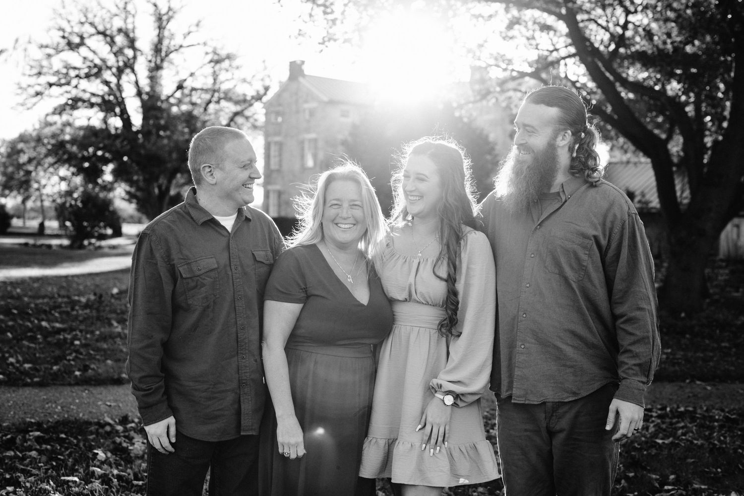 A family of four poses together outdoors in black and white on an autumn day.