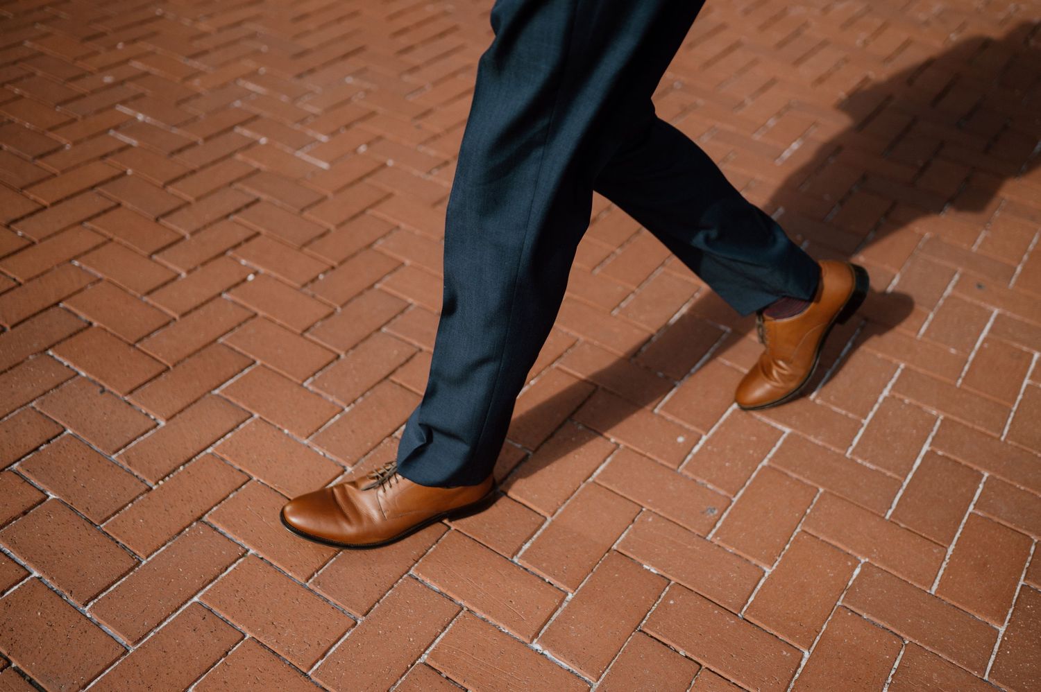 Close-up of dress shoes and suit pants walking on brick pavement.