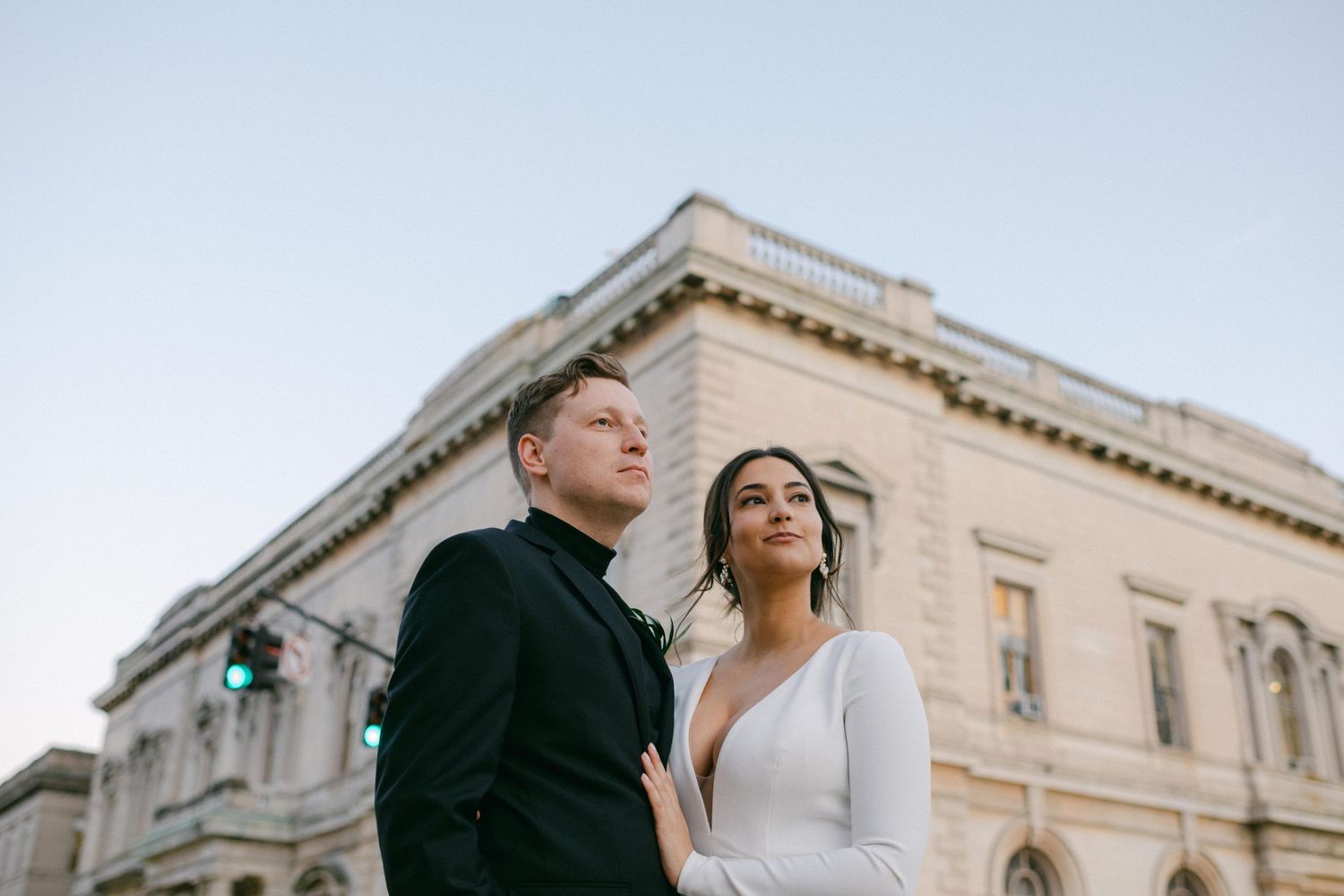Elegant couple in black and white attire pose together against classic stone building exterior.