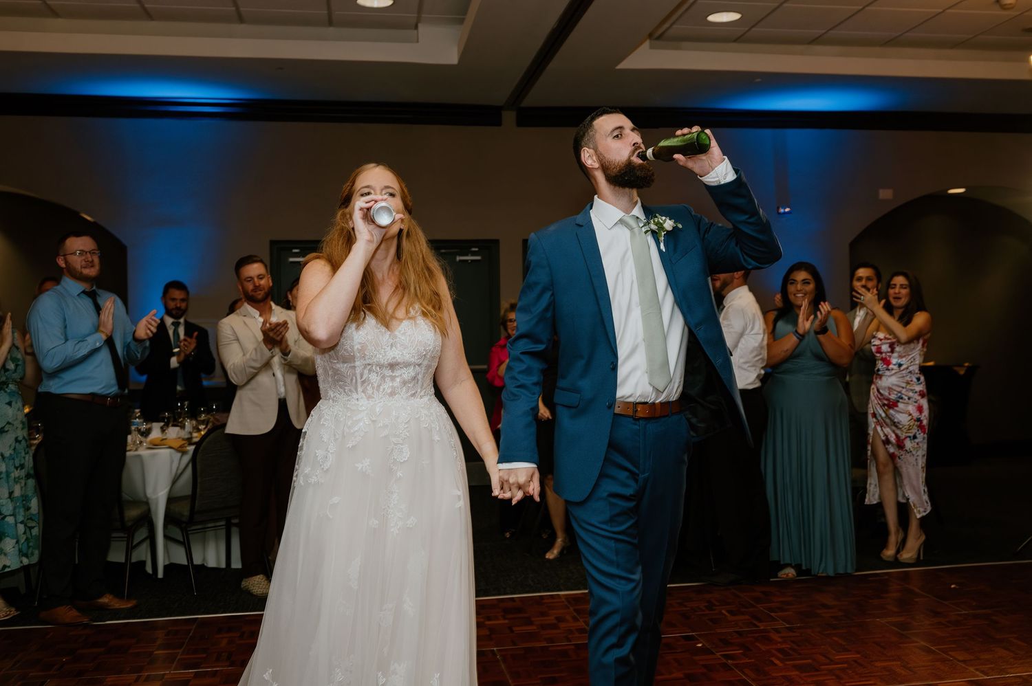 Wedding couple taking a celebratory drink together on the dance floor while guests watch.
